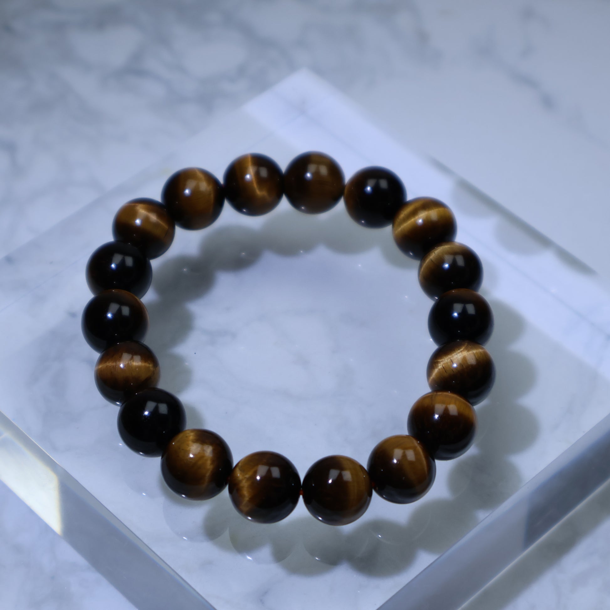 Top-down view of Tiger’s Eye bracelet on clear acrylic block, showing golden-brown chatoyance