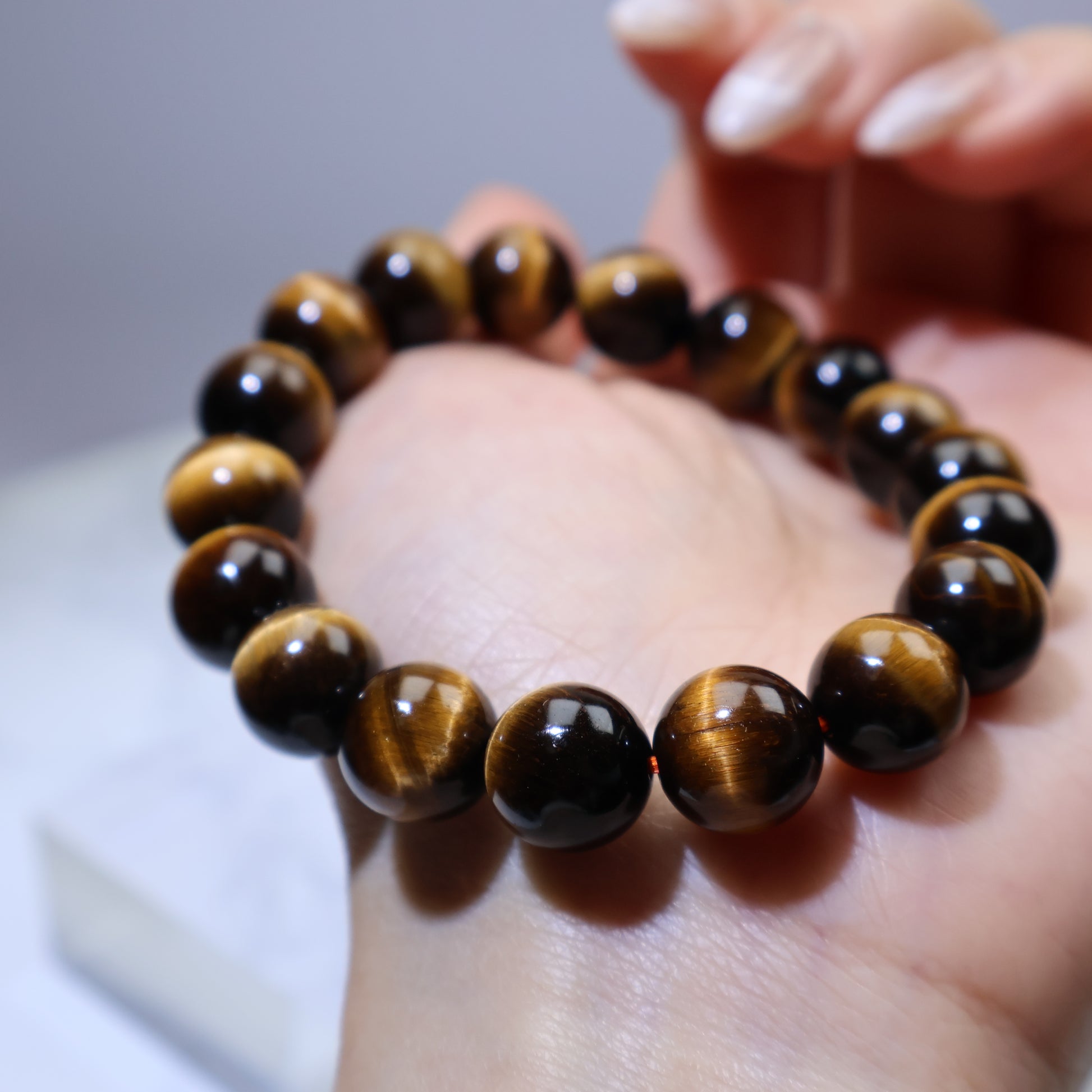 Angled view of Tiger’s Eye bracelet in hand, showing reflective chatoyancy under light