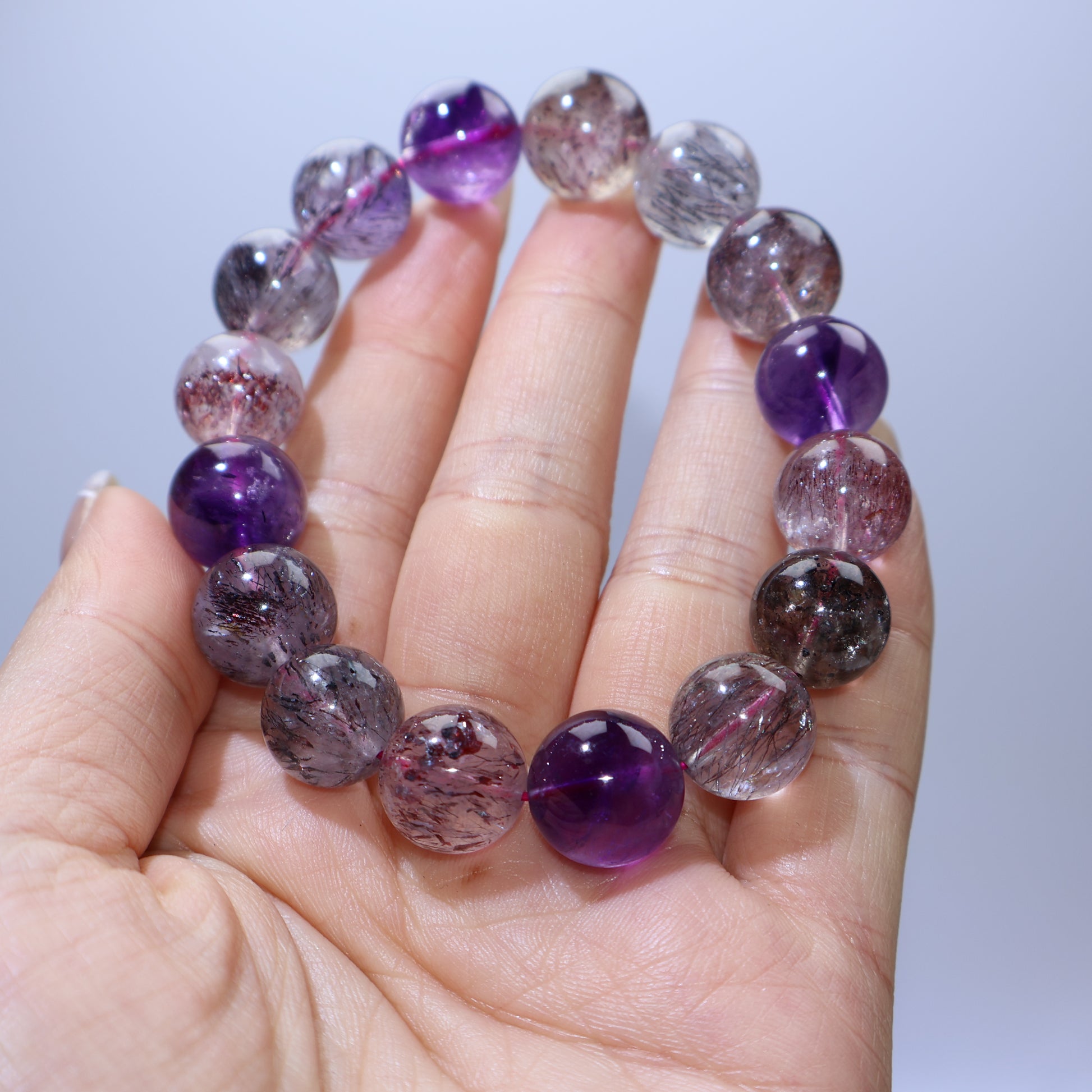 Handheld view of 12.8–13.5mm Super Seven beads with lepidocrocite/cacoxenite needles