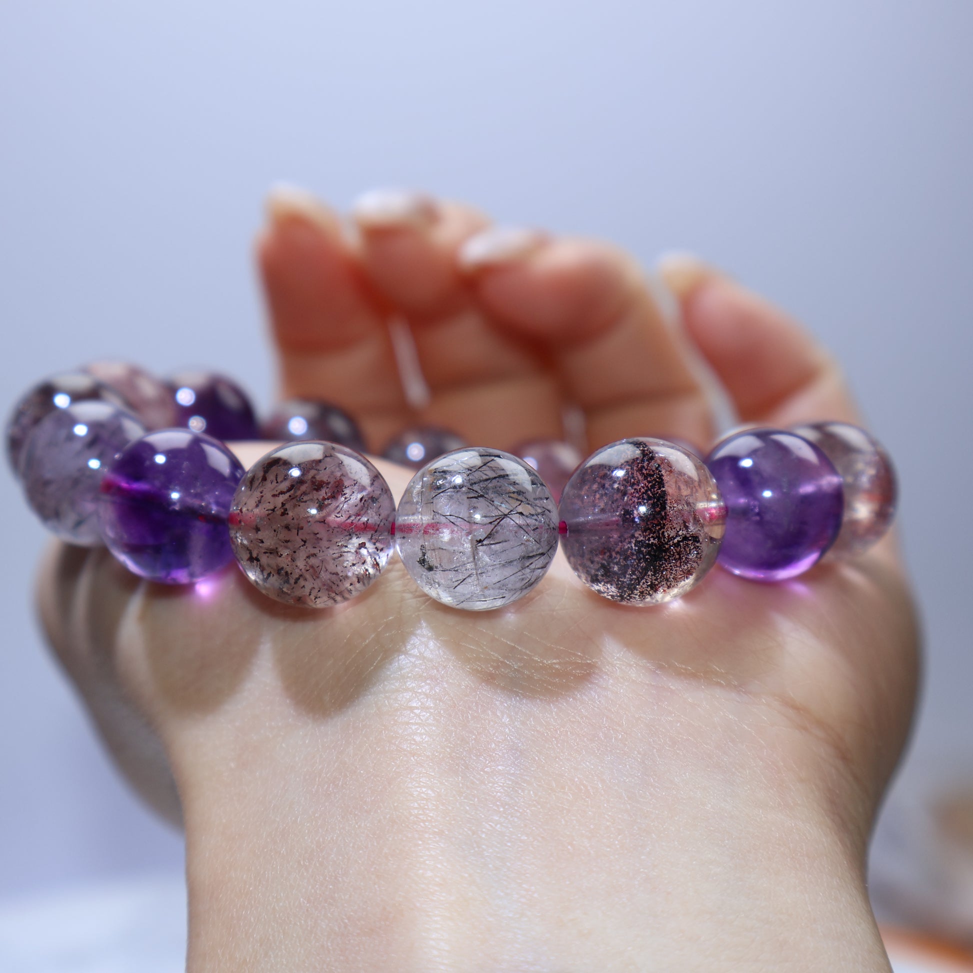 Row-on-palm macro showing clear beads with fine rutile-like needles and cottony veils