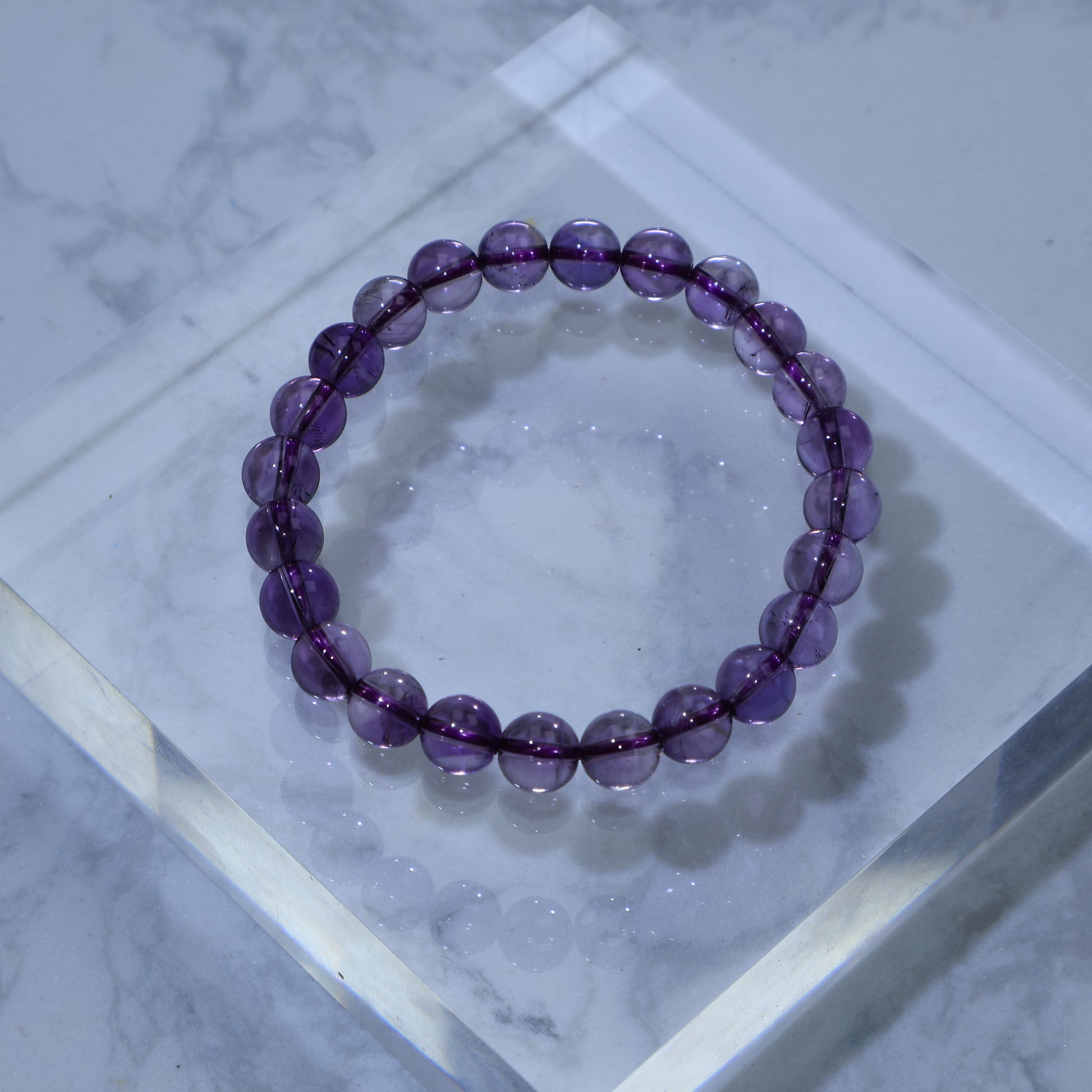 Overhead view of 7mm Amethyst bracelet on clear acrylic block, showing soft violet tones