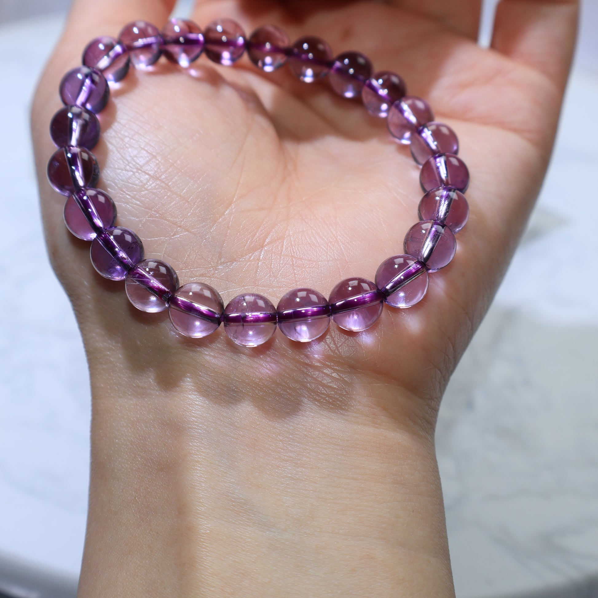 Wrist shot under bright light, beads glowing with subtle lavender hues