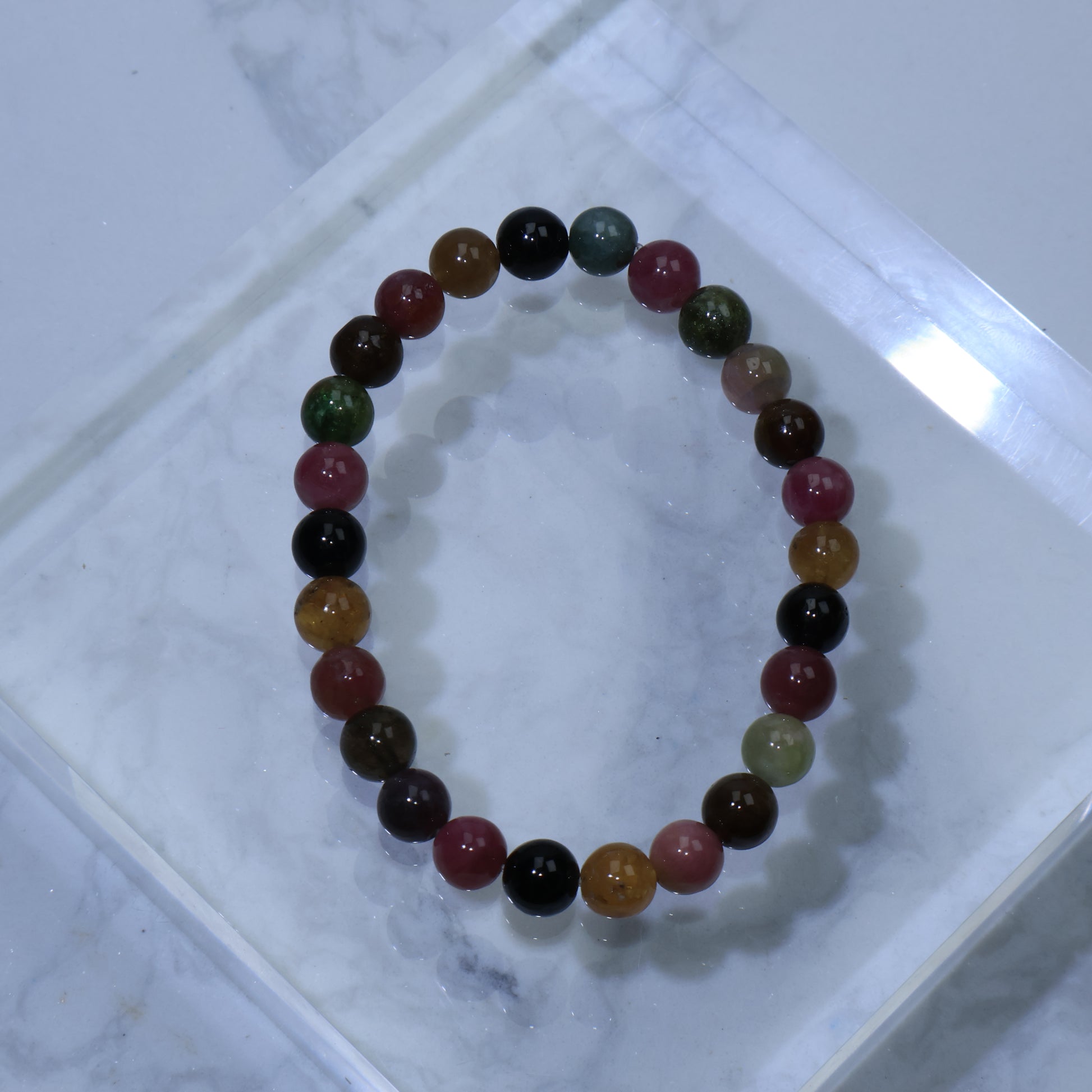 Overhead view of 7mm Multicolor Tourmaline bracelet on clear acrylic block, showing vibrant mix of pink, green, yellow, blue, and black beads