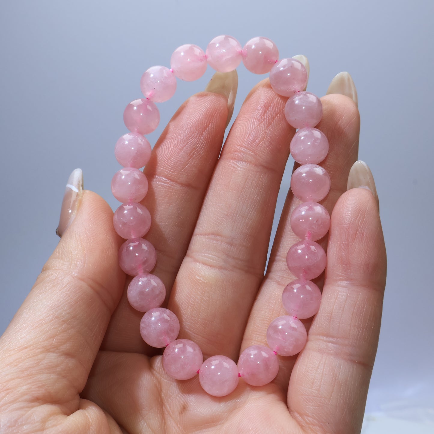 Close-up of Madagascar Rose Quartz bracelet held in hand, showing uniform blush-pink color and natural inclusions.