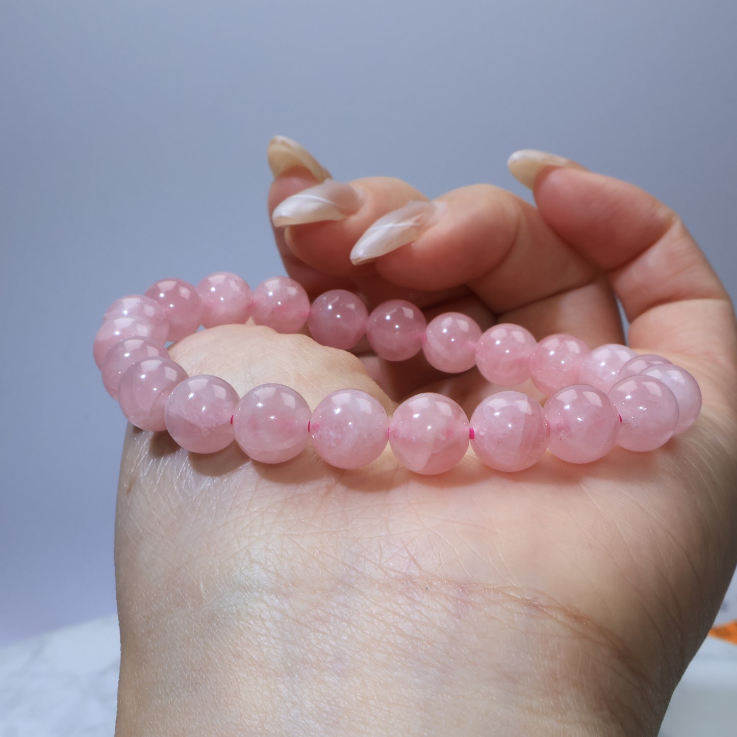 Side-angle shot of Madagascar Rose Quartz bracelet cradled in hand, highlighting polished surface and soft pink tone.