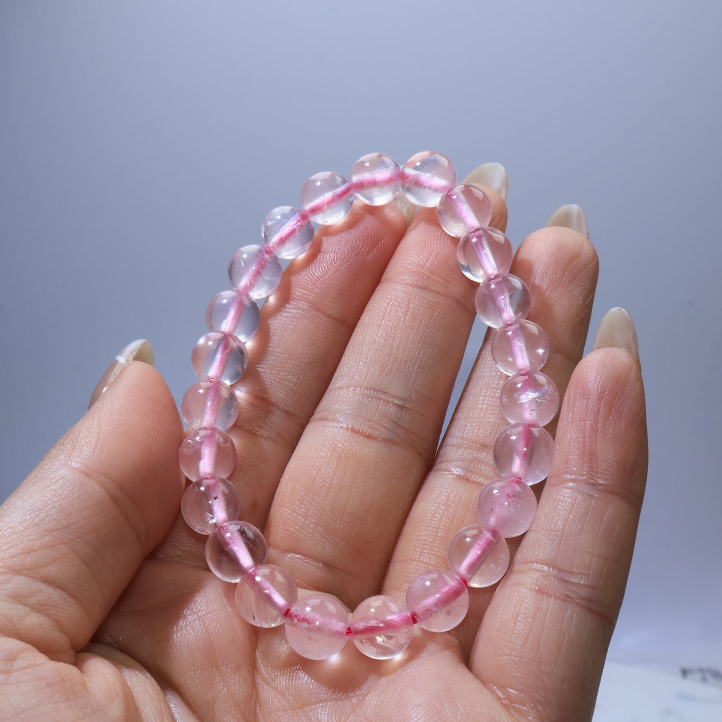 Handheld view of Rose Quartz bracelet, highlighting clear beads with blush-pink tones and visible ice cracks.