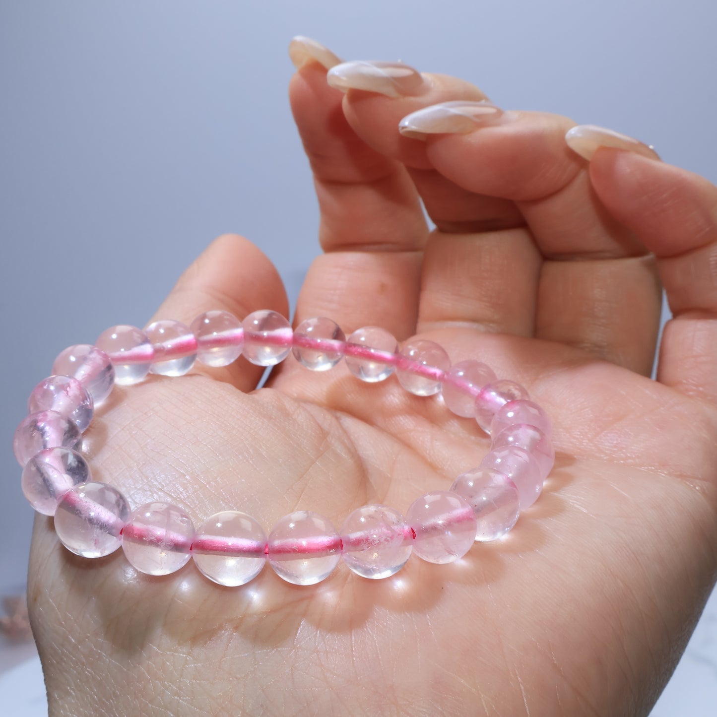 Side-angle shot of Rose Quartz bracelet resting in hand, emphasizing its smooth polish and gentle pink color.