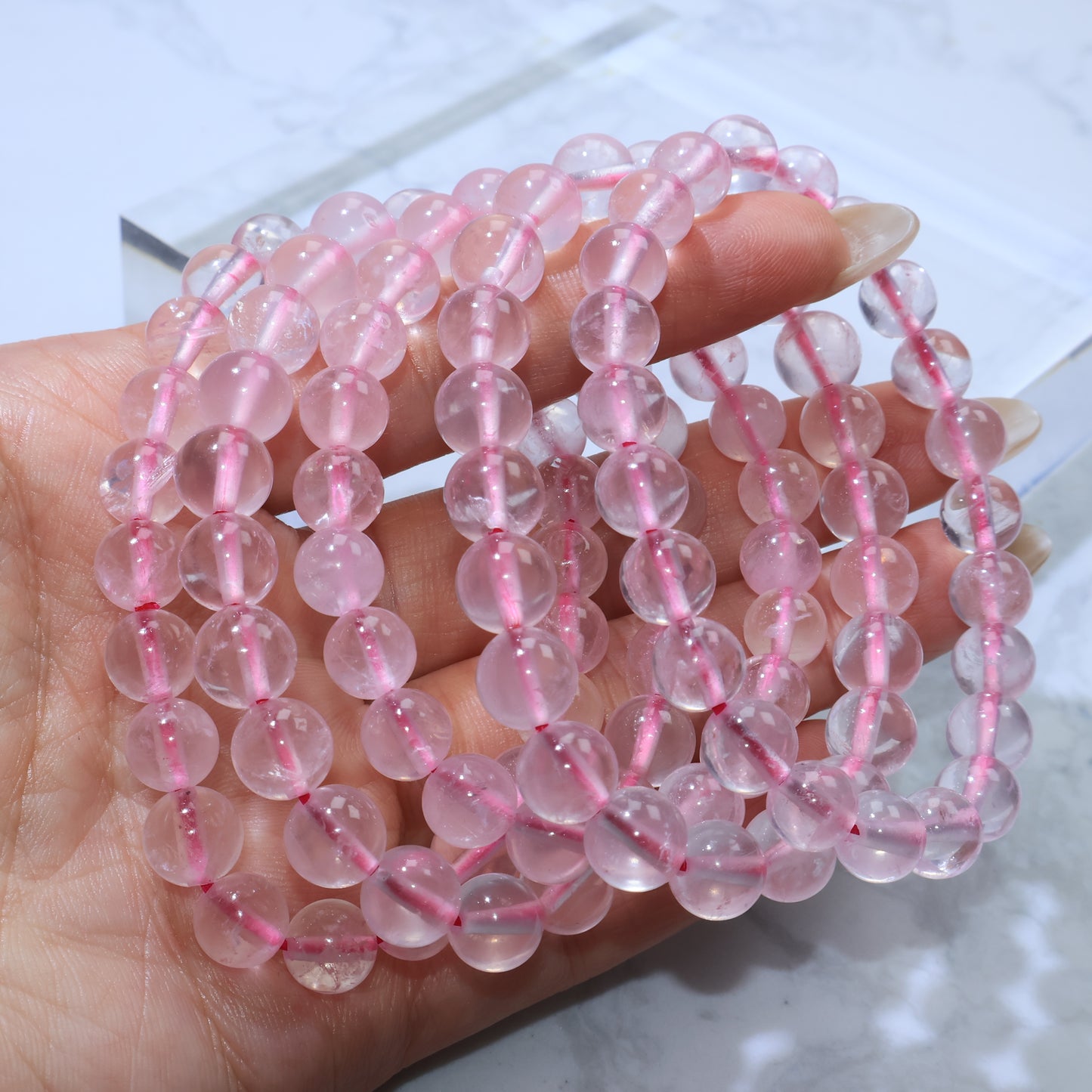 Multiple Rose Quartz bracelets stacked together in hand, showcasing uniform bead size and soft romantic tone.