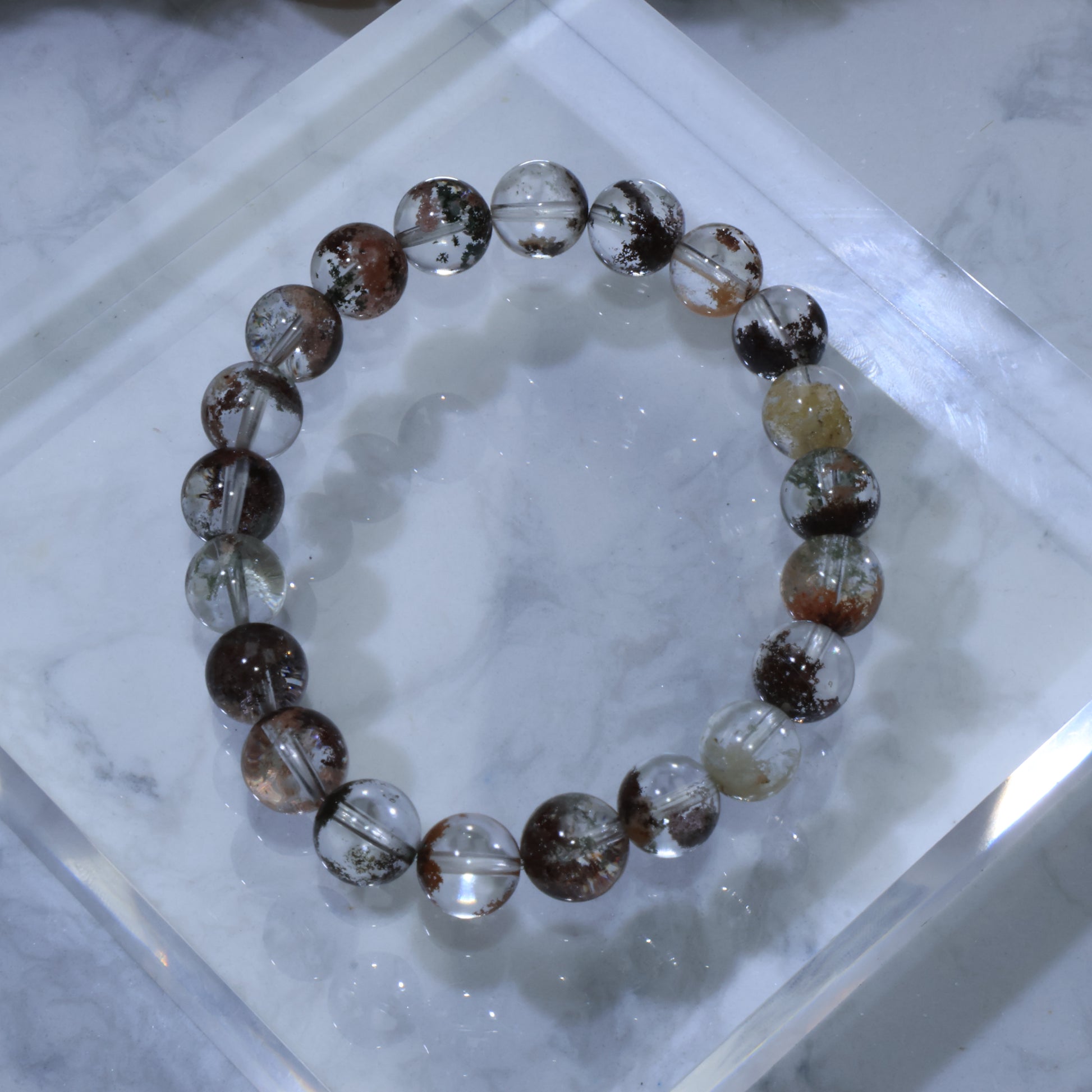 Top-down view of Scenic Phantom Quartz bracelet with clear crystals and multicolored phantom inclusions on acrylic display