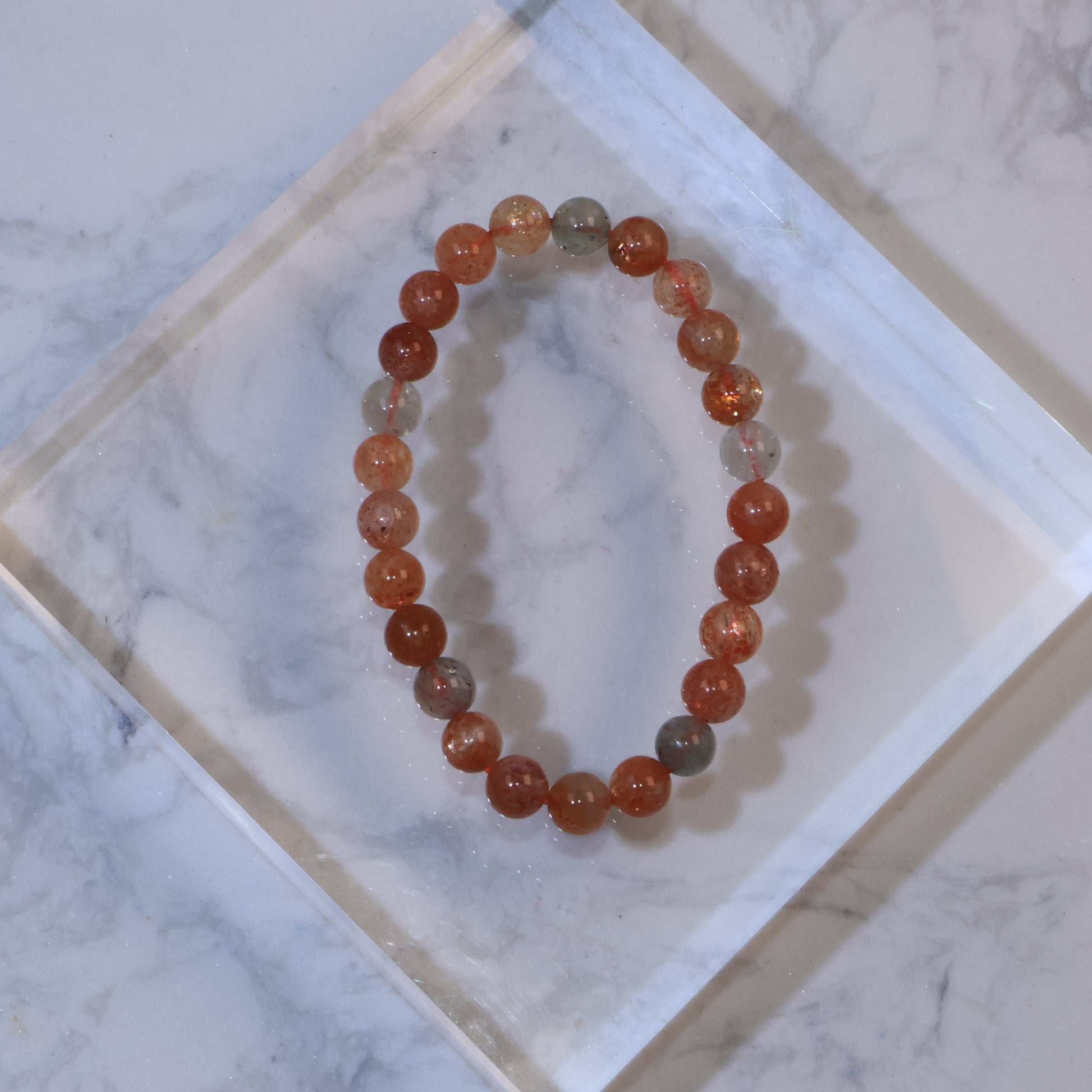 Top view of Arusha Sunstone bracelet with reddish-orange beads on clear acrylic block