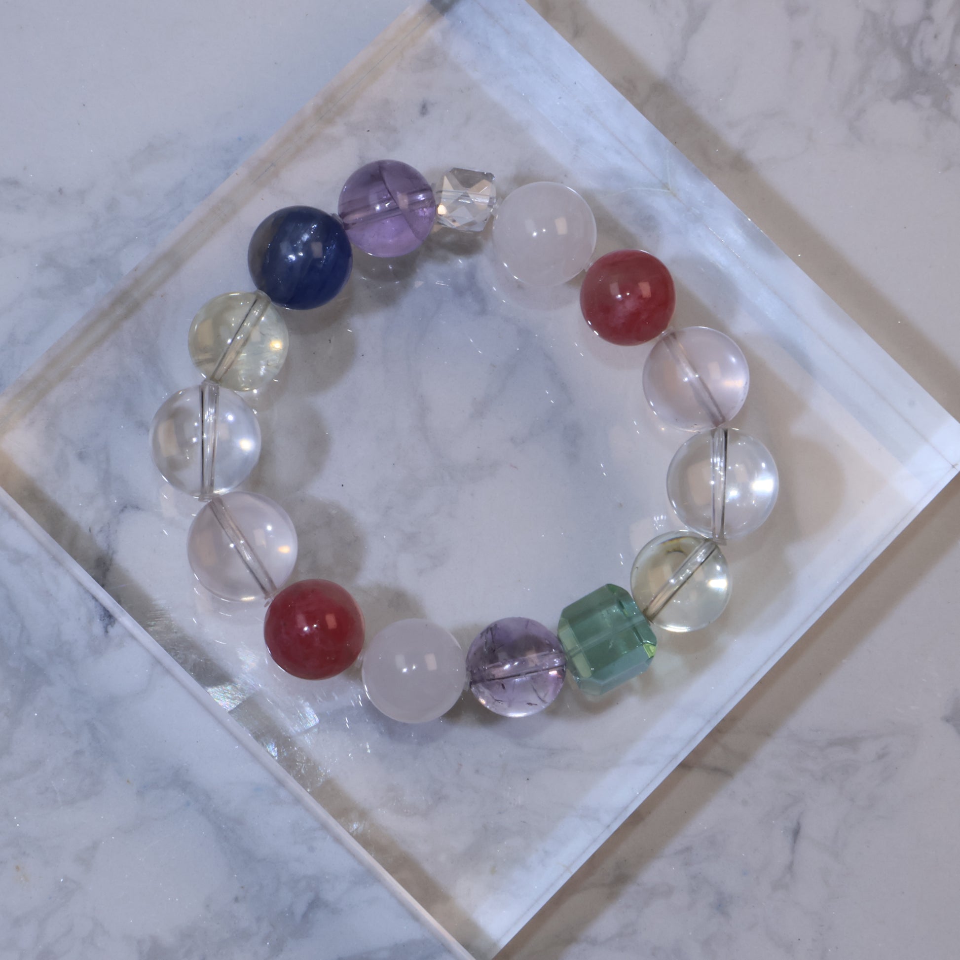 Top-down view of multicolored gemstone bracelet with round and square beads on a marble surface