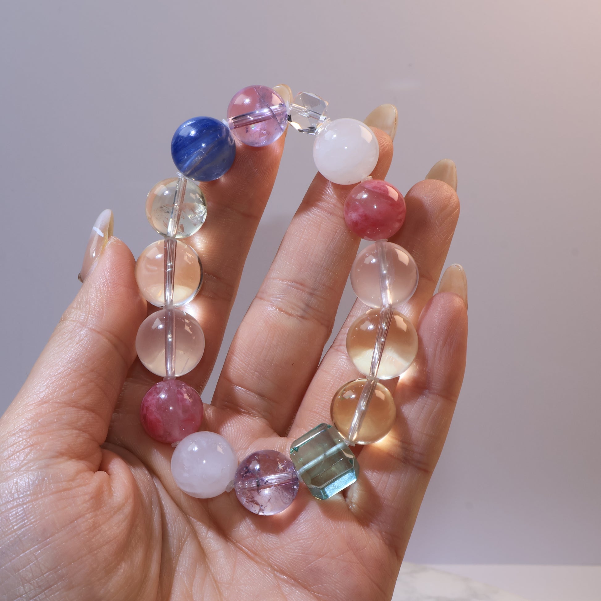 Hand holding multicolored gemstone bracelet showing blue kyanite, amethyst, citrine, and green fluorite