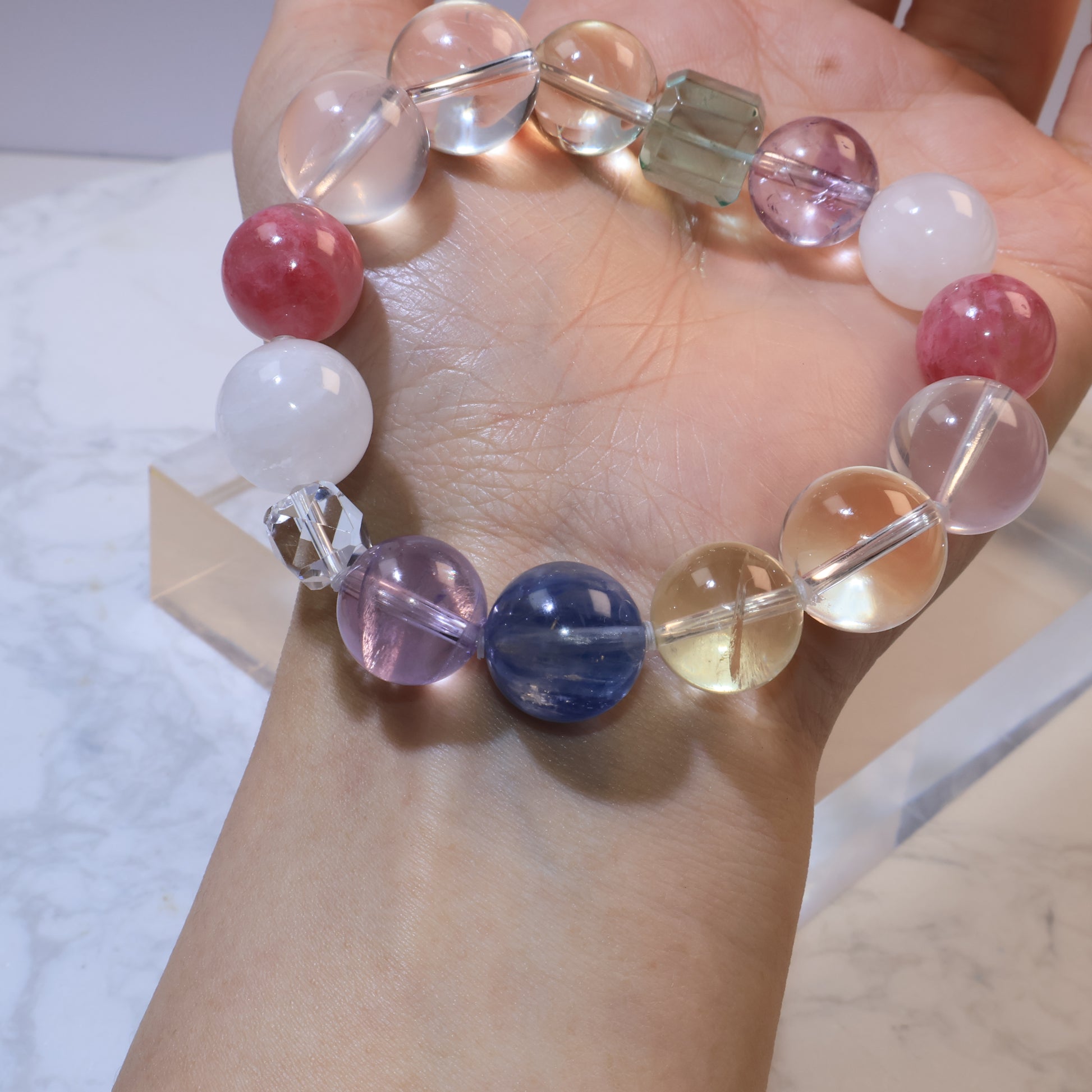 Close-up wrist shot showing red rhodochrosite, rose quartz, and clear quartz faceted bead