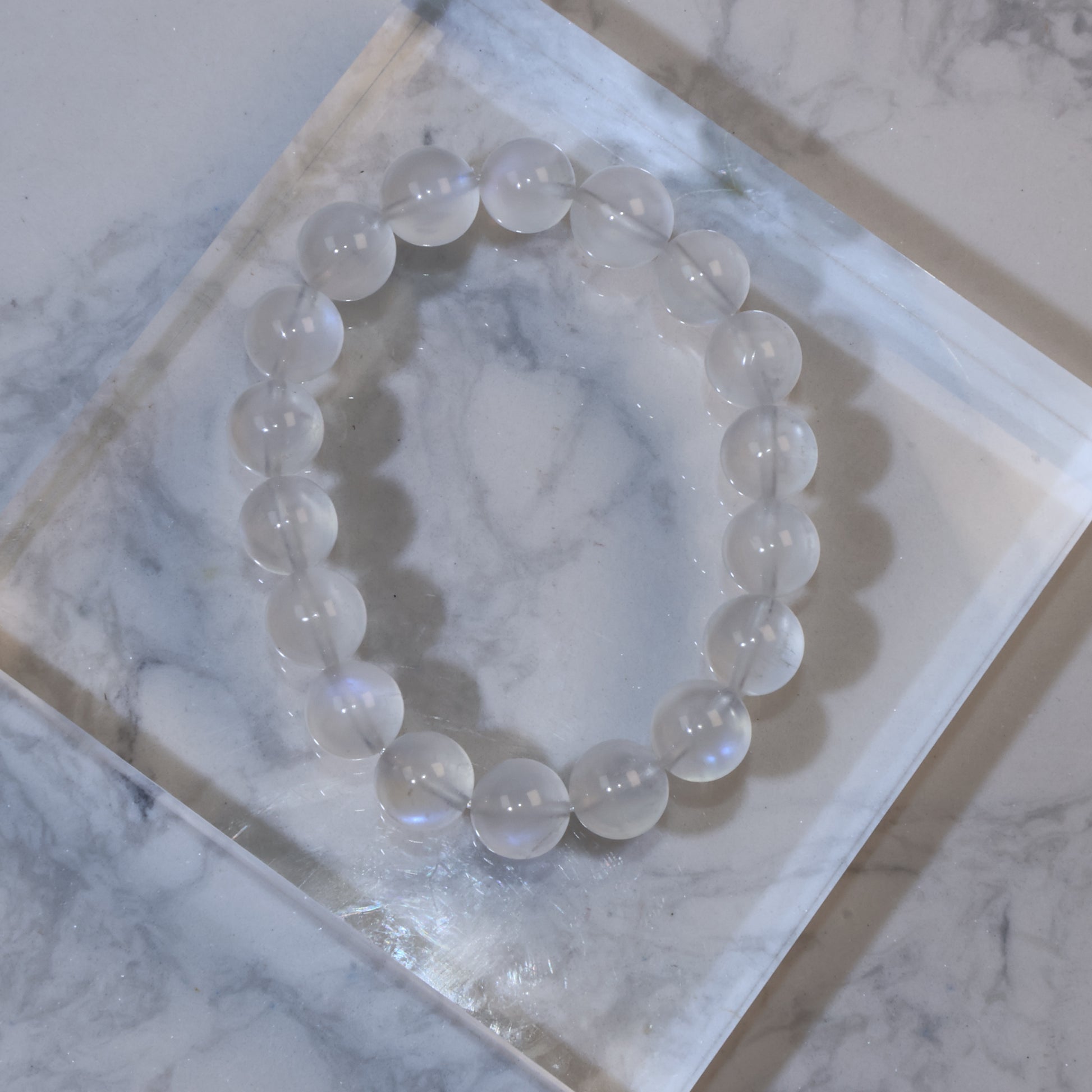 Top view of 11mm moonstone bracelet on clear acrylic block, showing soft milky translucence and blue sheen