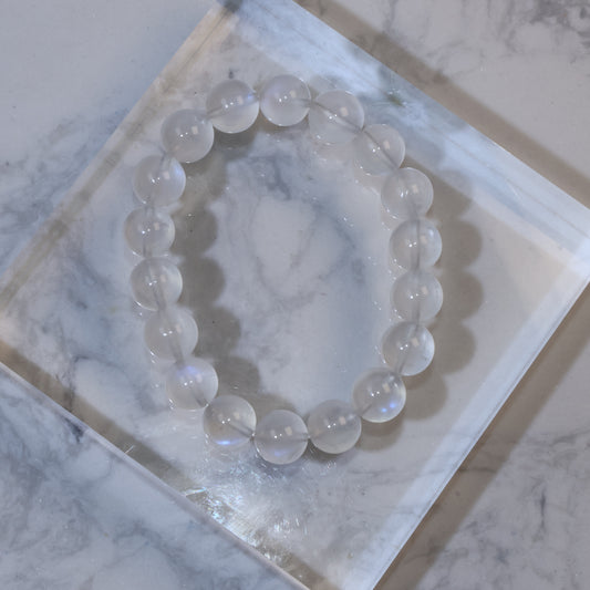 Top view of 11mm moonstone bracelet on clear acrylic block, showing soft milky translucence and blue sheen