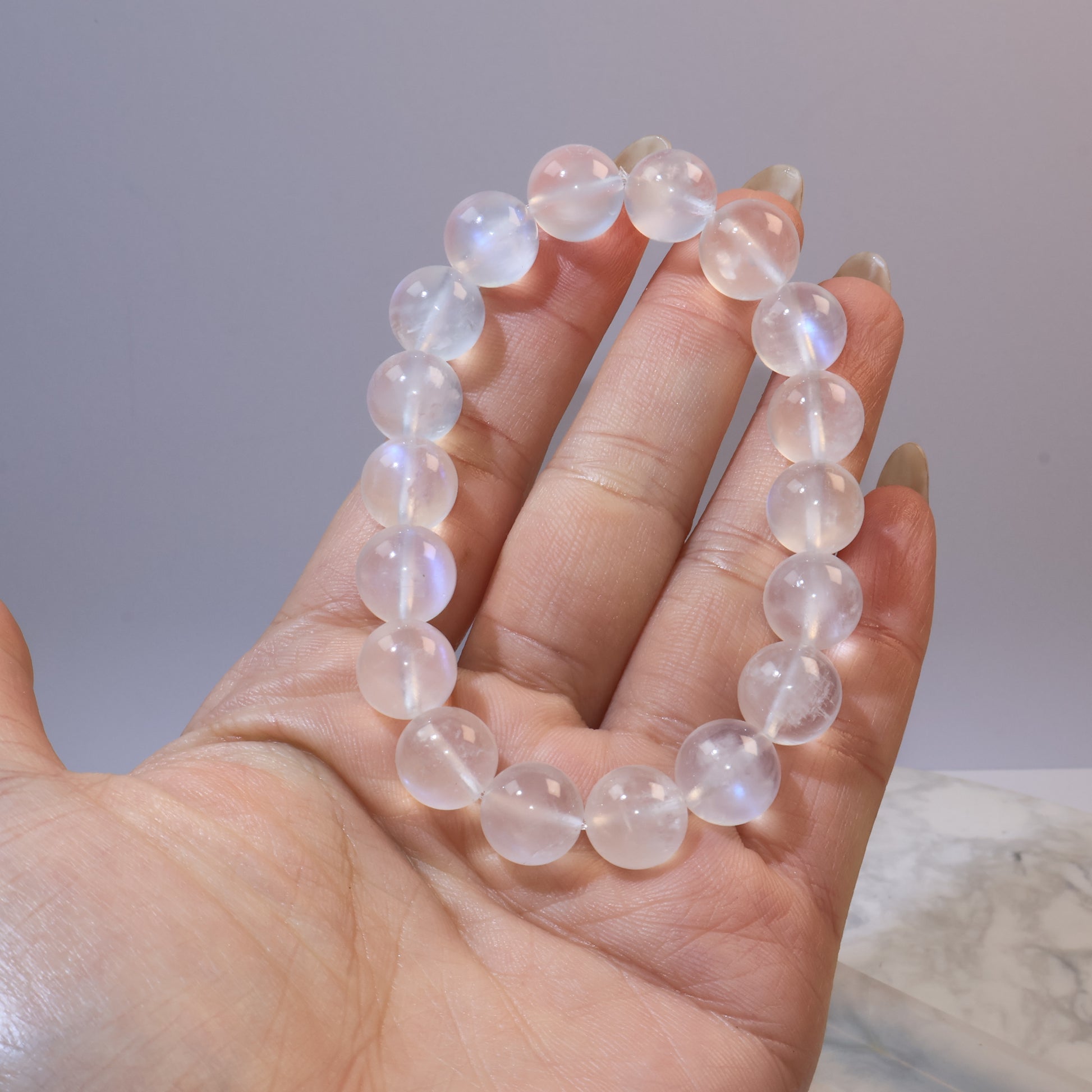 Hand holding 11mm moonstone bracelet, beads reflecting blue flashes under light
