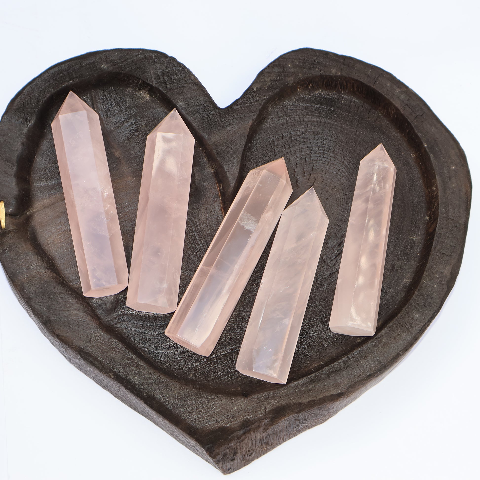 English: Set of five rose quartz towers arranged on a heart-shaped wooden tray, glowing with soft pink energy.