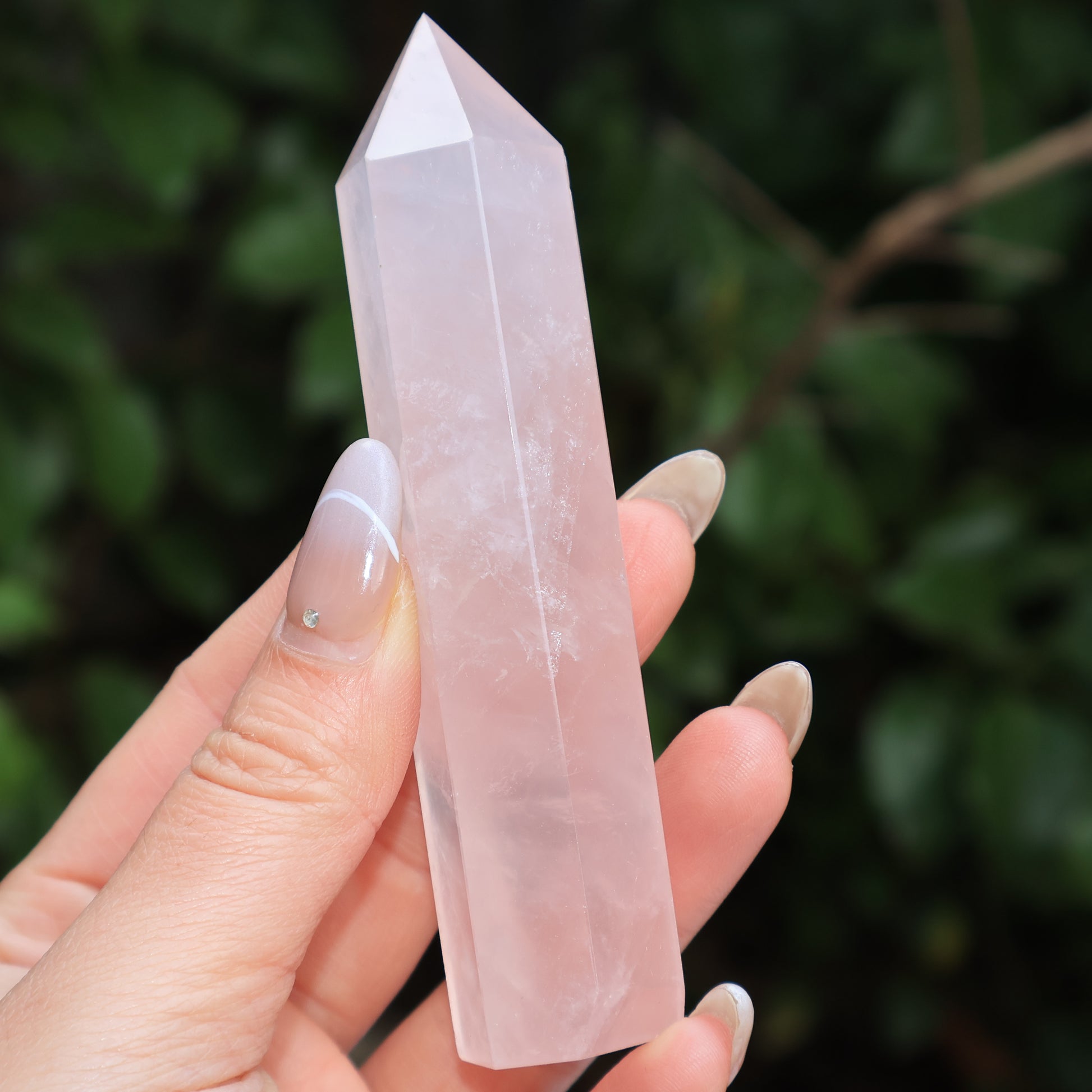 Close-up of a hand holding a single rose quartz tower from the 5-piece set, showing natural clarity and inclusions.
