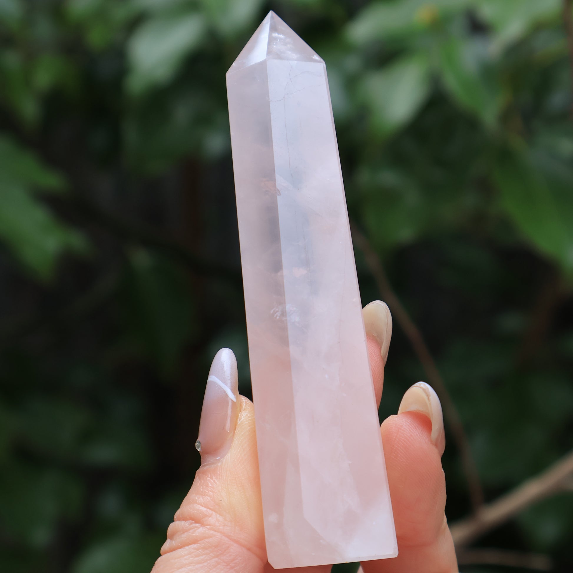 Tall rose quartz tower crystal with a pointed tip, held between fingers, glowing softly in sunlight.