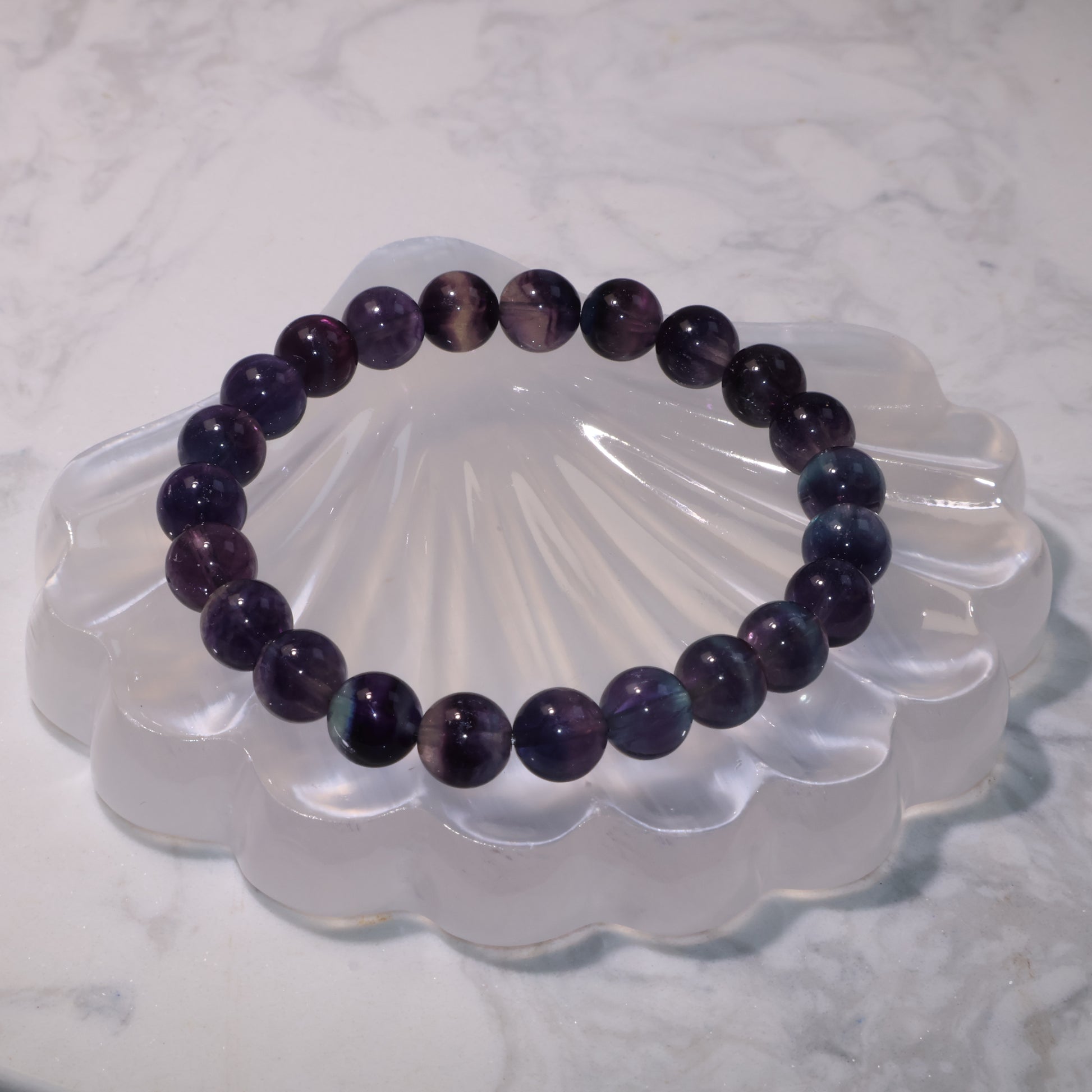 Fluorite bracelet 8mm beads in deep purple and blue tones displayed on a crystal shell stand.