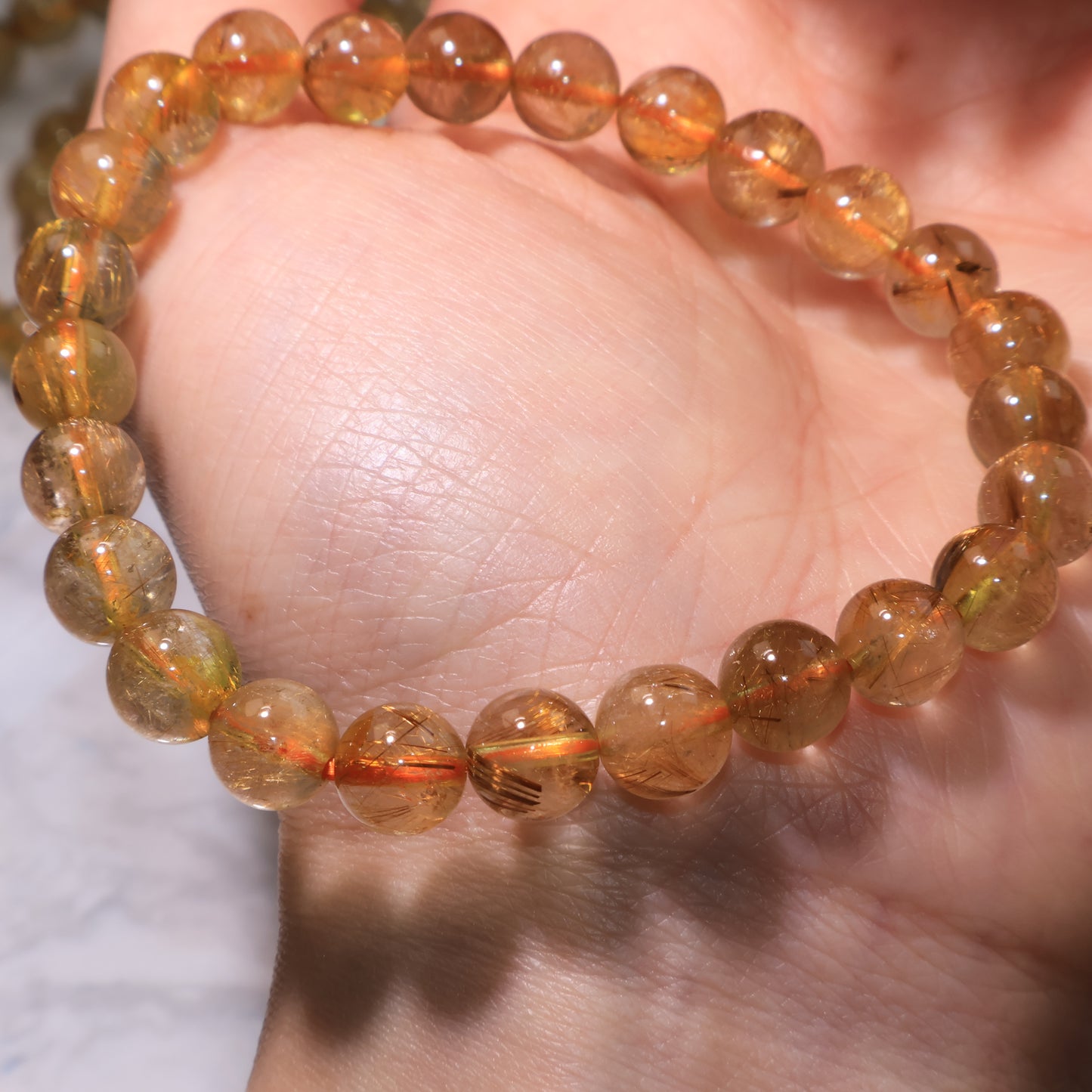 Close-up of Rutilated Quartz beads in the palm, glowing under light.