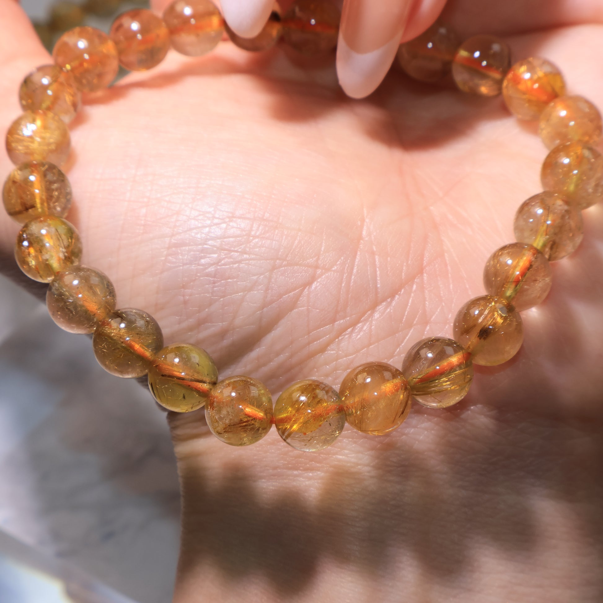 Golden-red rutile threads visible in round quartz beads, resting on palm.
