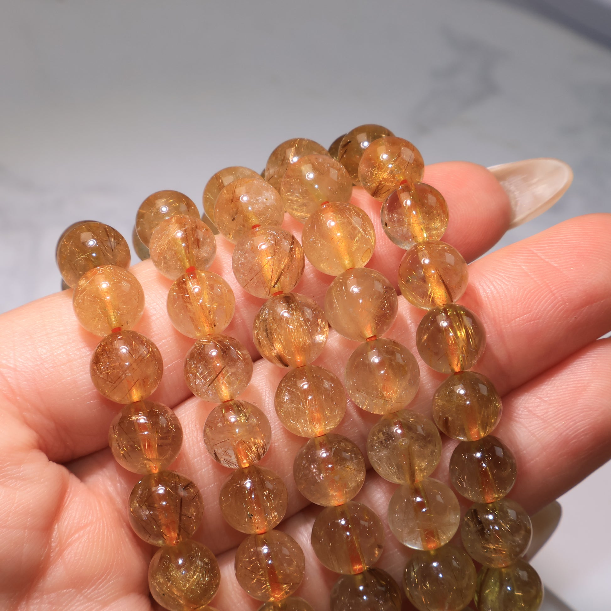 Several Golden Red Rutilated Quartz bracelets stacked together, showing varied rutile patterns.