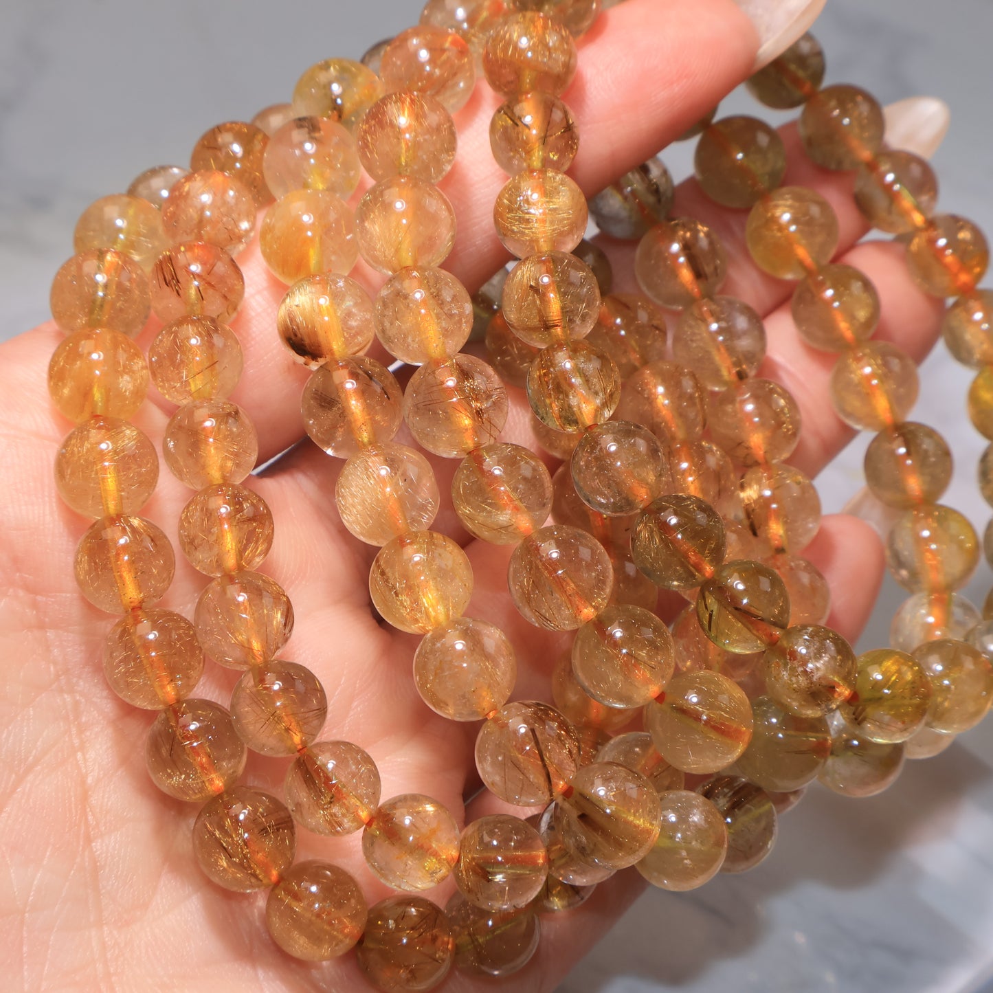 Close-up of multiple Rutilated Quartz bracelets, each with unique rutile inclusions.
