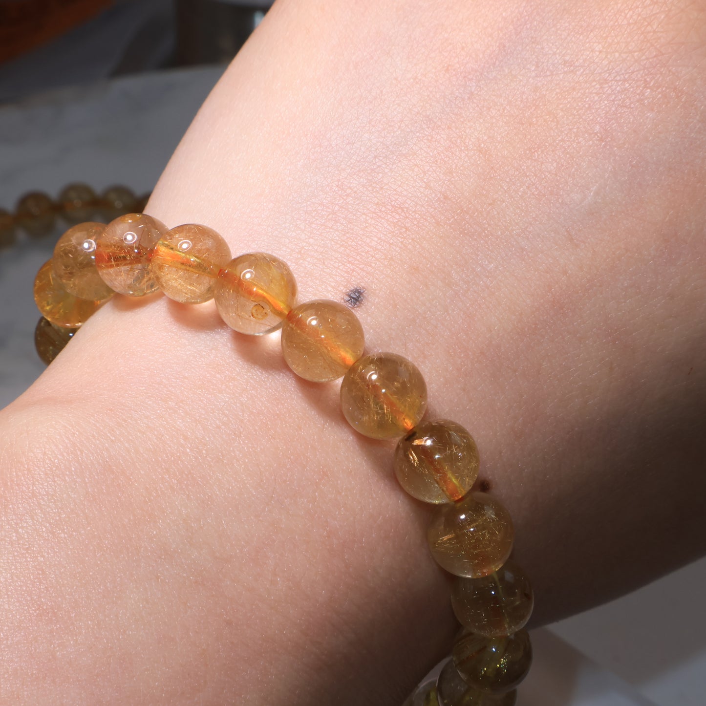 Golden Red Rutilated Quartz bracelet worn on wrist, transparent beads reflecting warm glow.