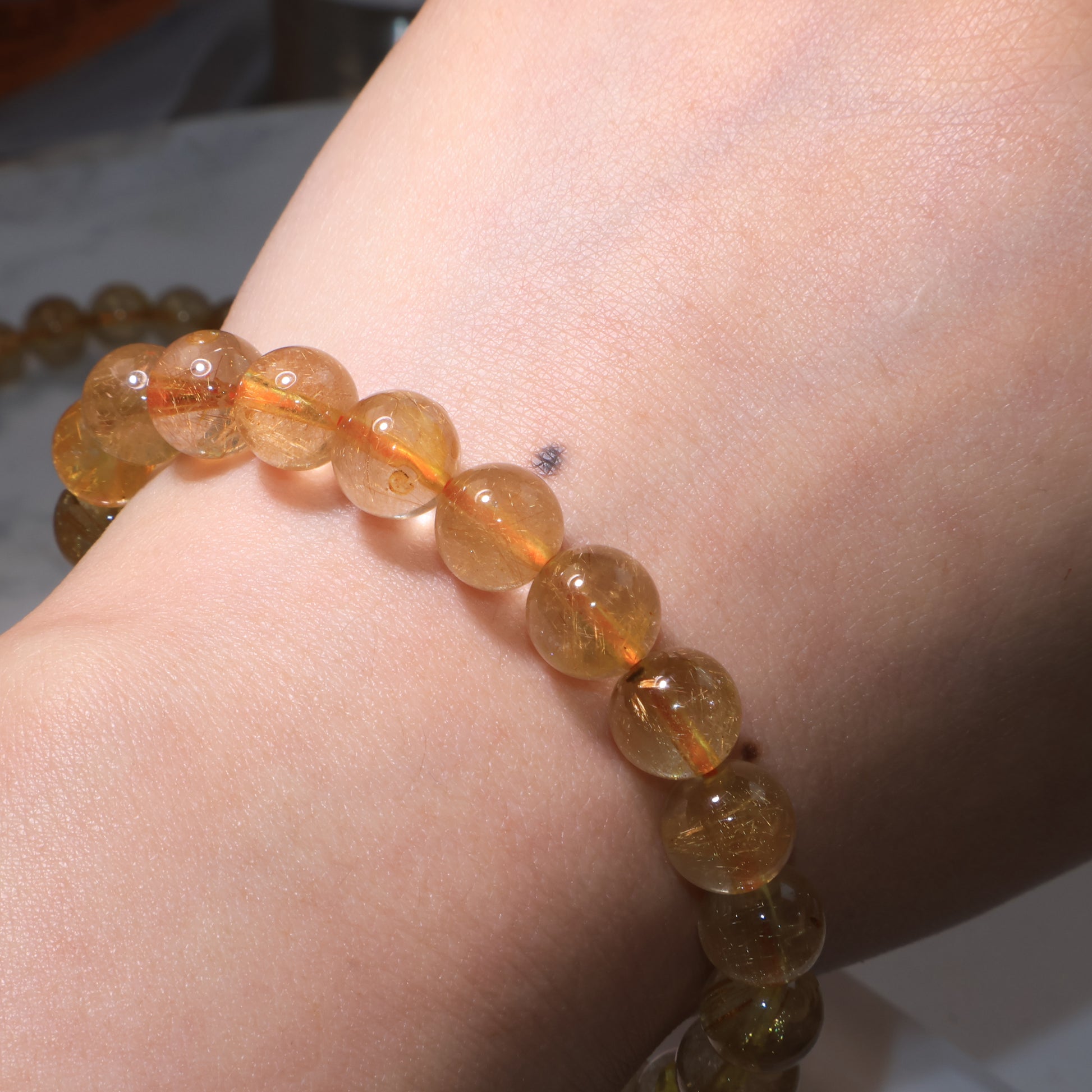 Golden Red Rutilated Quartz bracelet worn on wrist, transparent beads reflecting warm glow.