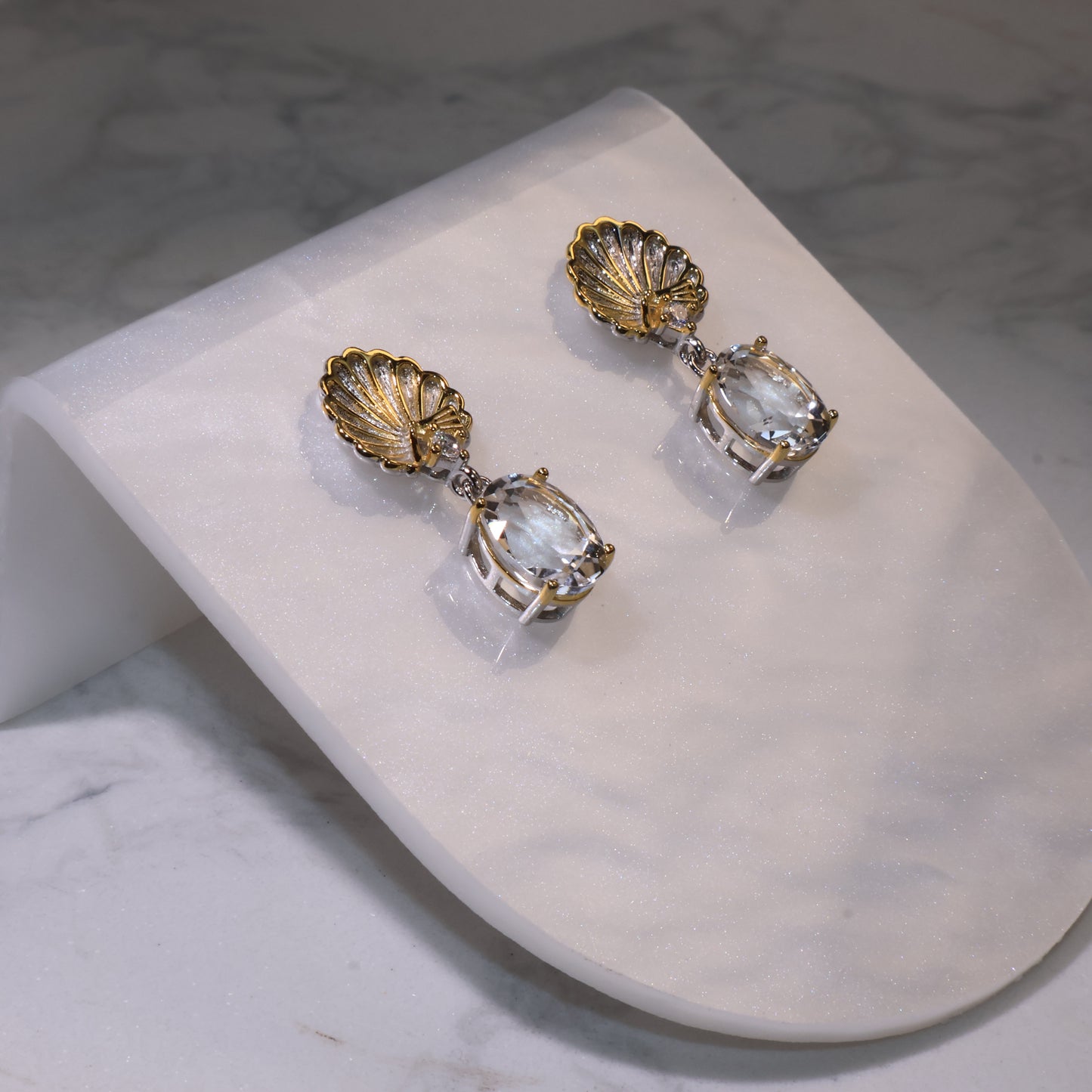 Side angle view showing the oval-cut clear quartz and shell design with silver-gold details.
