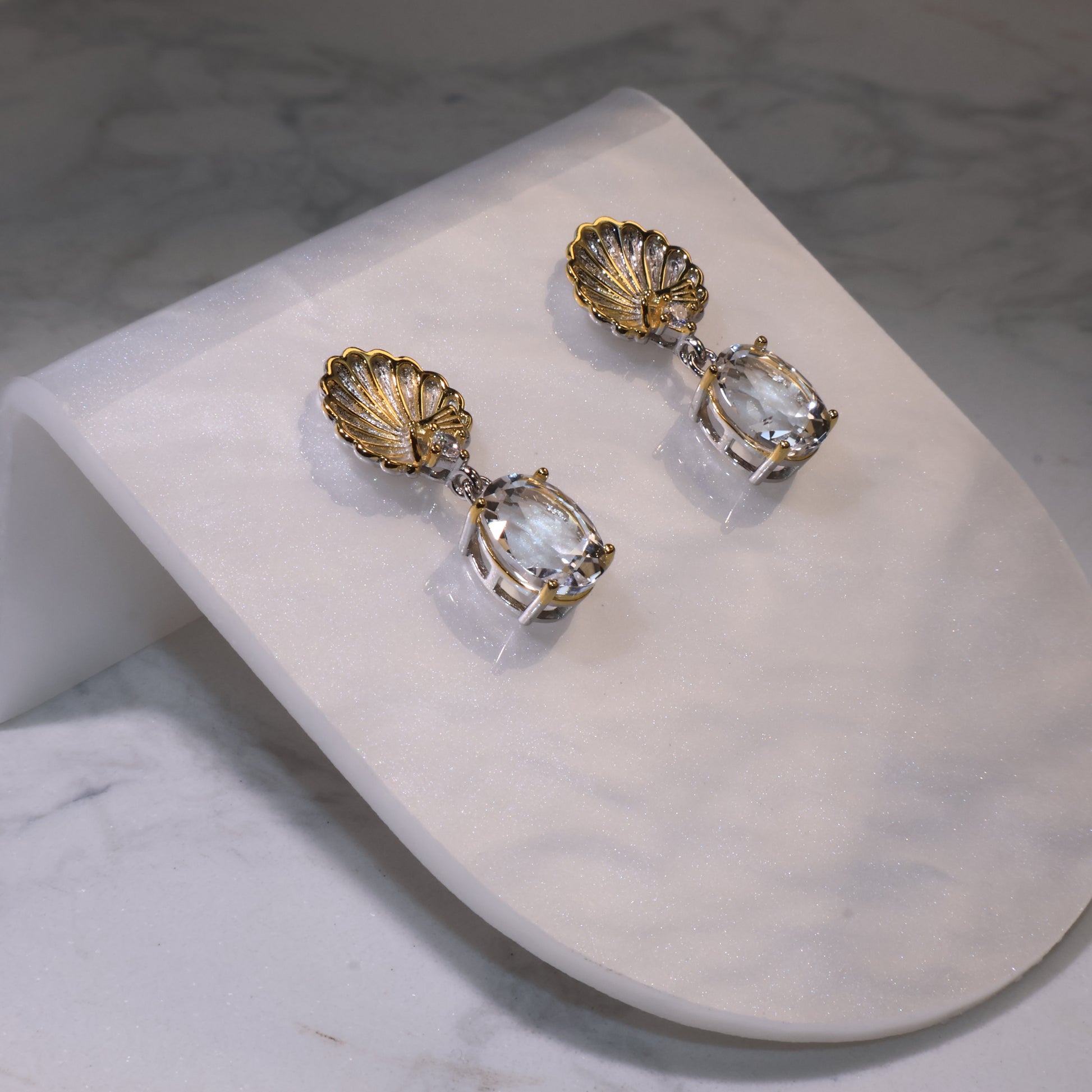 Side angle view showing the oval-cut clear quartz and shell design with silver-gold details.