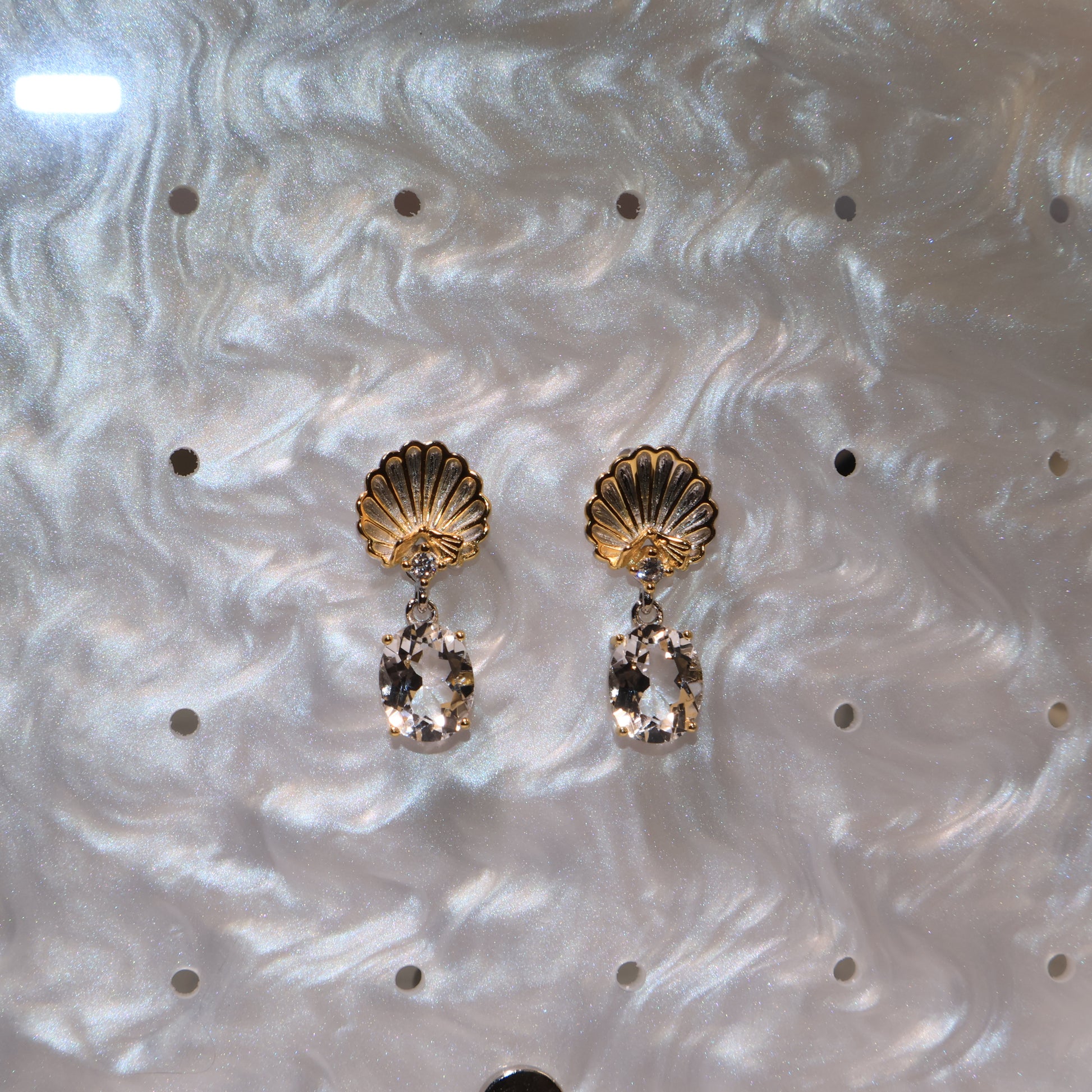 Earrings under soft lighting showing the shimmering gold and the reflective quartz surface.