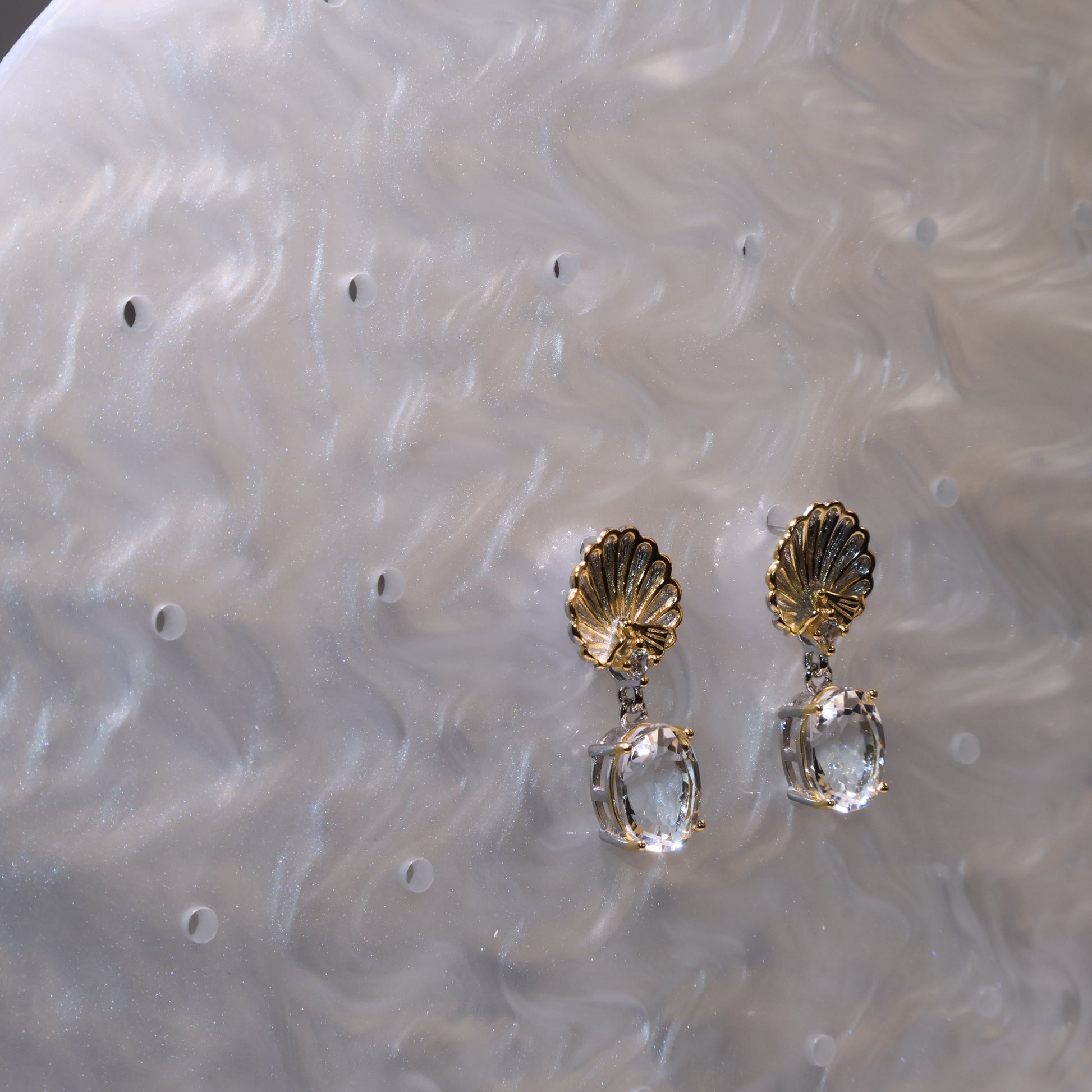 Earrings photographed from a side view with the pearl-pattern background glimmering softly.