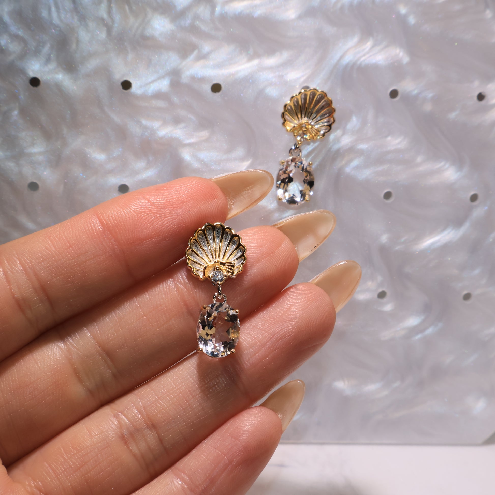 Hand holding one earring to show size, craftsmanship, and the sparkle of clear quartz.