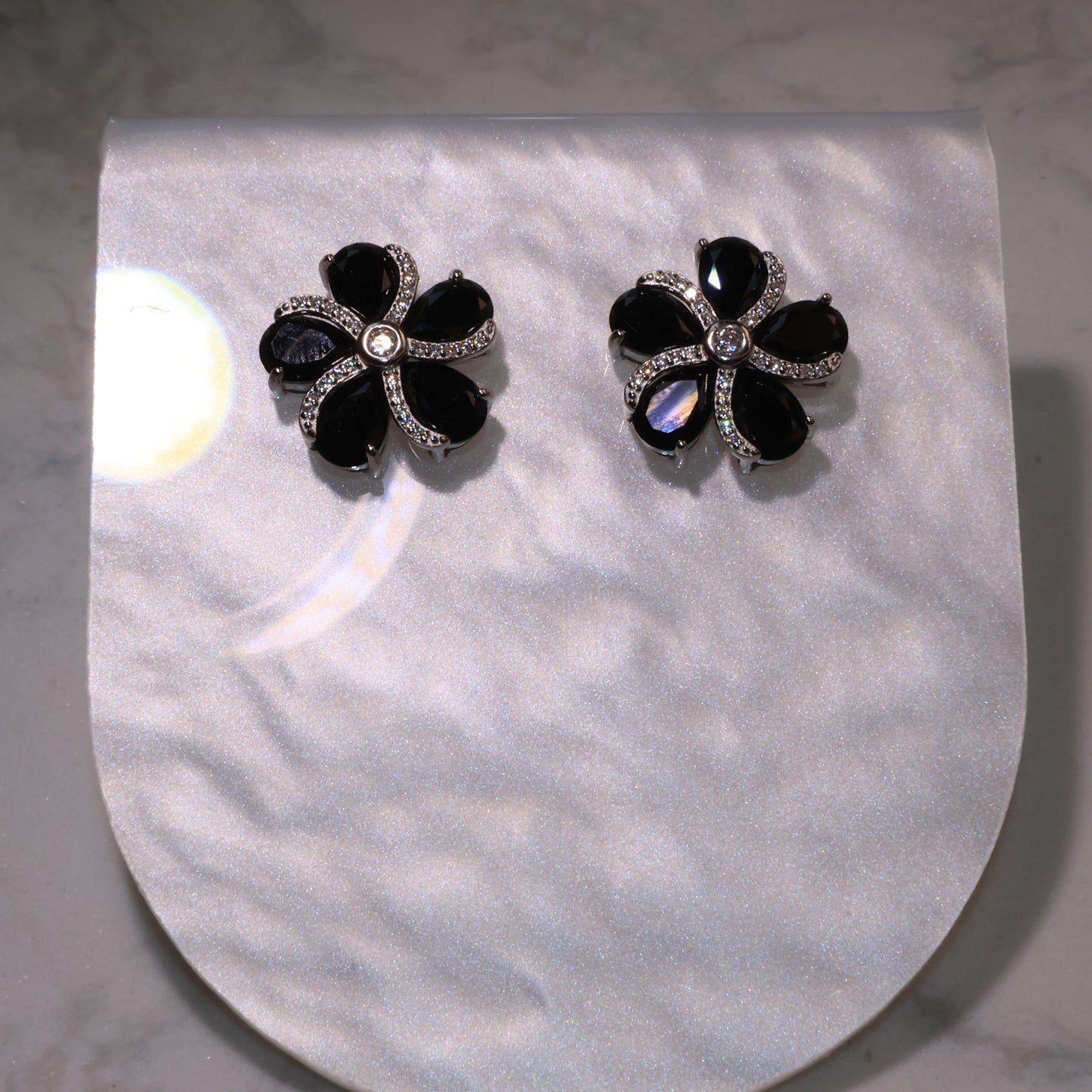 pair of black spinel flower earrings with zircon accents displayed on a pearly background.