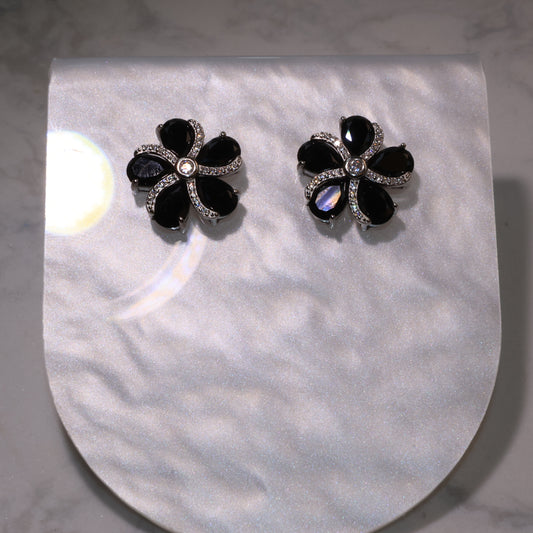 pair of black spinel flower earrings with zircon accents displayed on a pearly background.