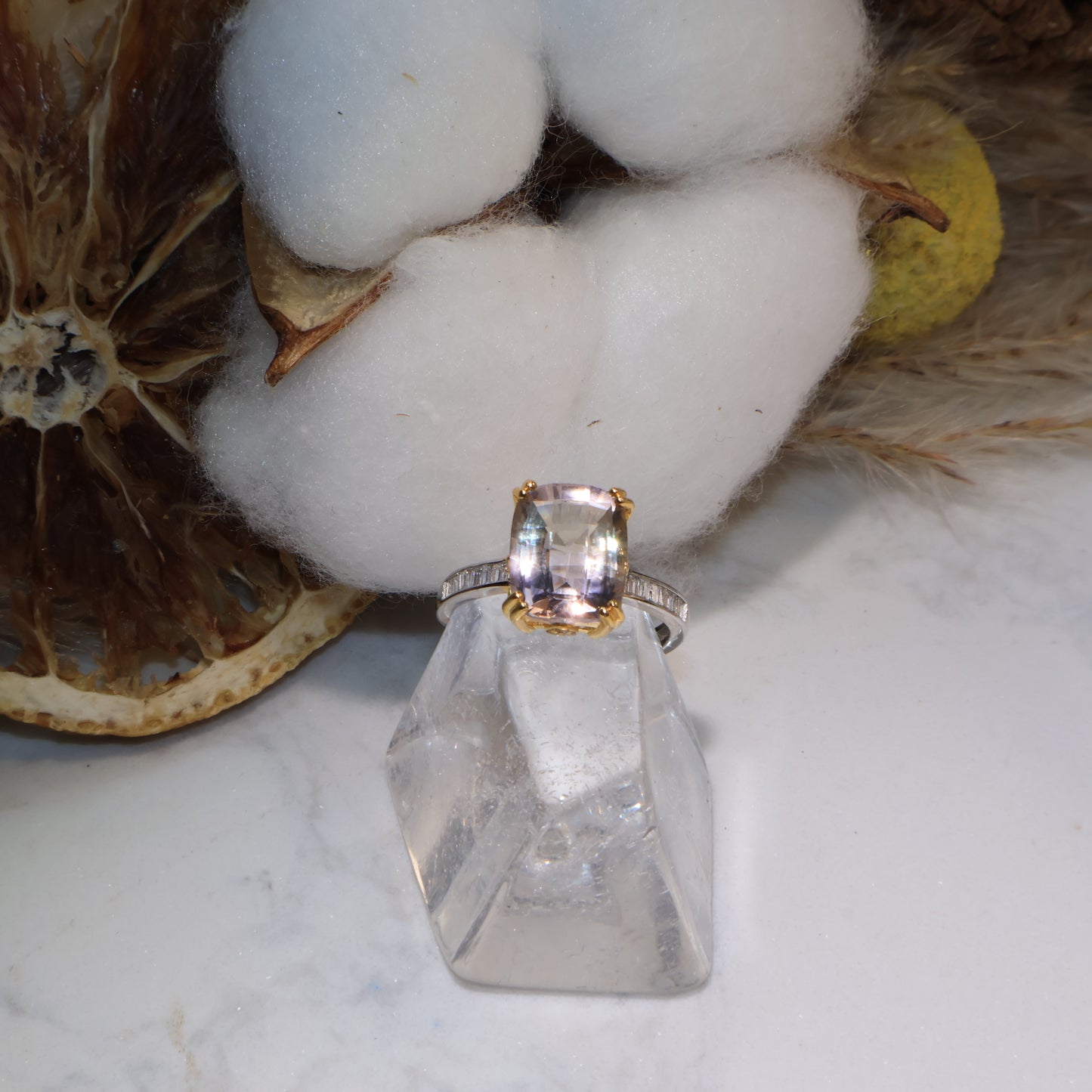 Close-up of an ametrine ring with soft purple and golden hues, displayed on a clear quartz stand with cotton background.