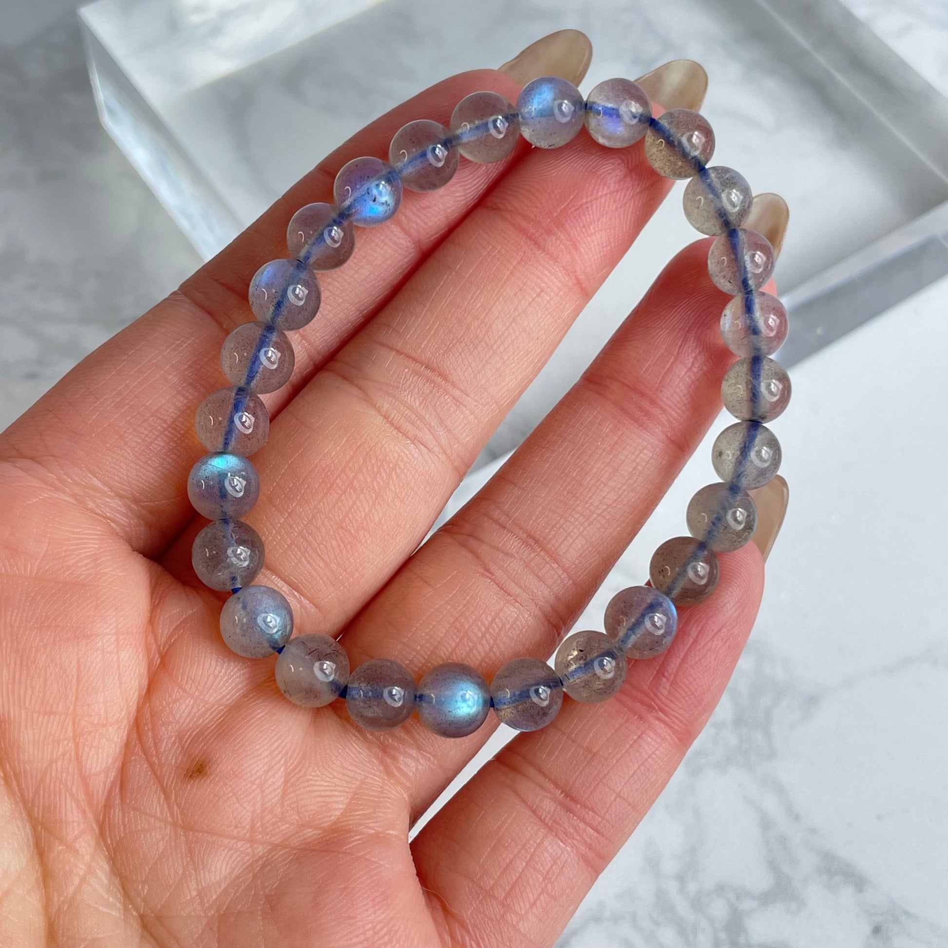 Labradorite glow bracelet with blue flashes – 6mm beads, from Madagascar. Displayed on hand and flat lay with marble background.
