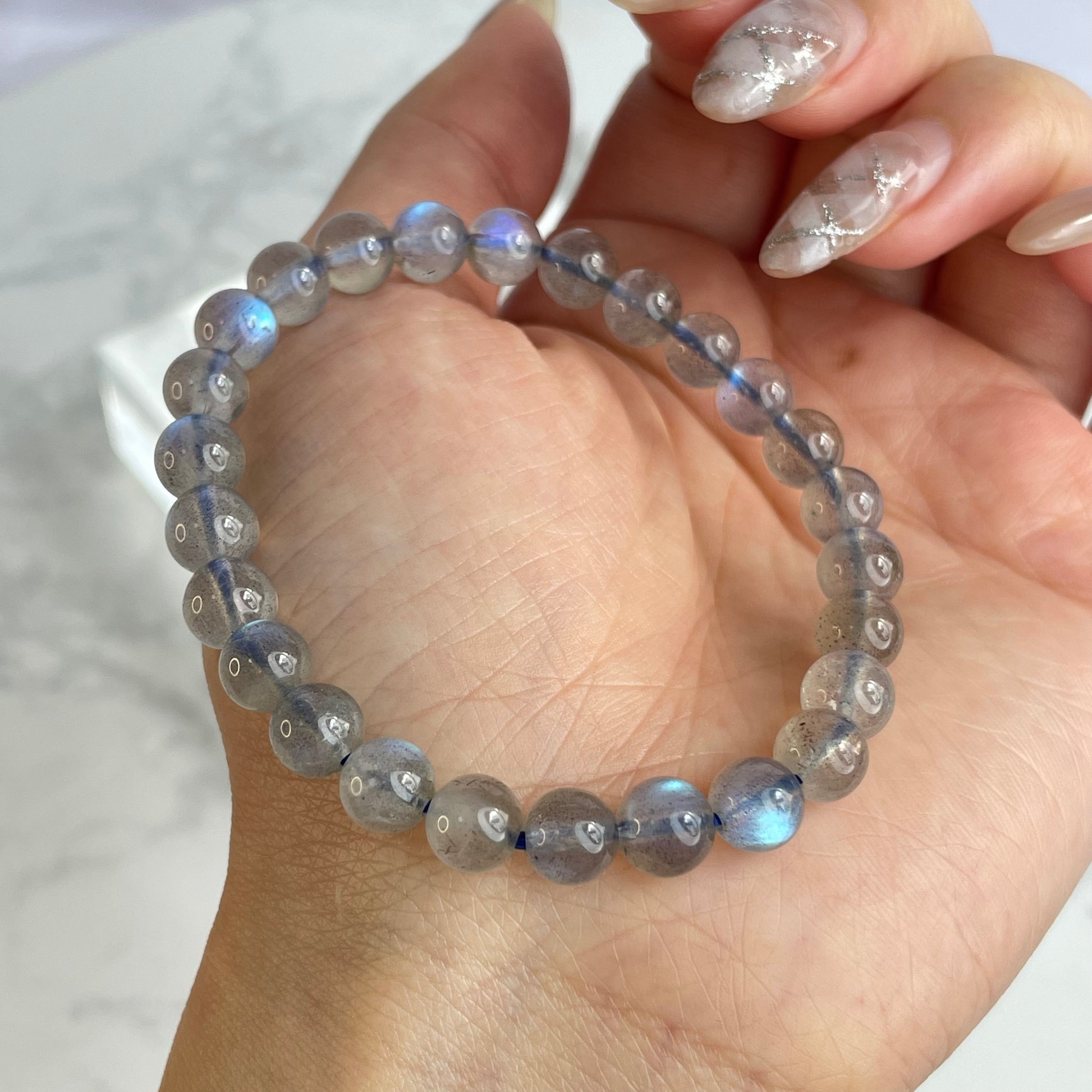 Labradorite glow bracelet with blue flashes – 6mm beads, from Madagascar. Displayed on hand and flat lay with marble background.