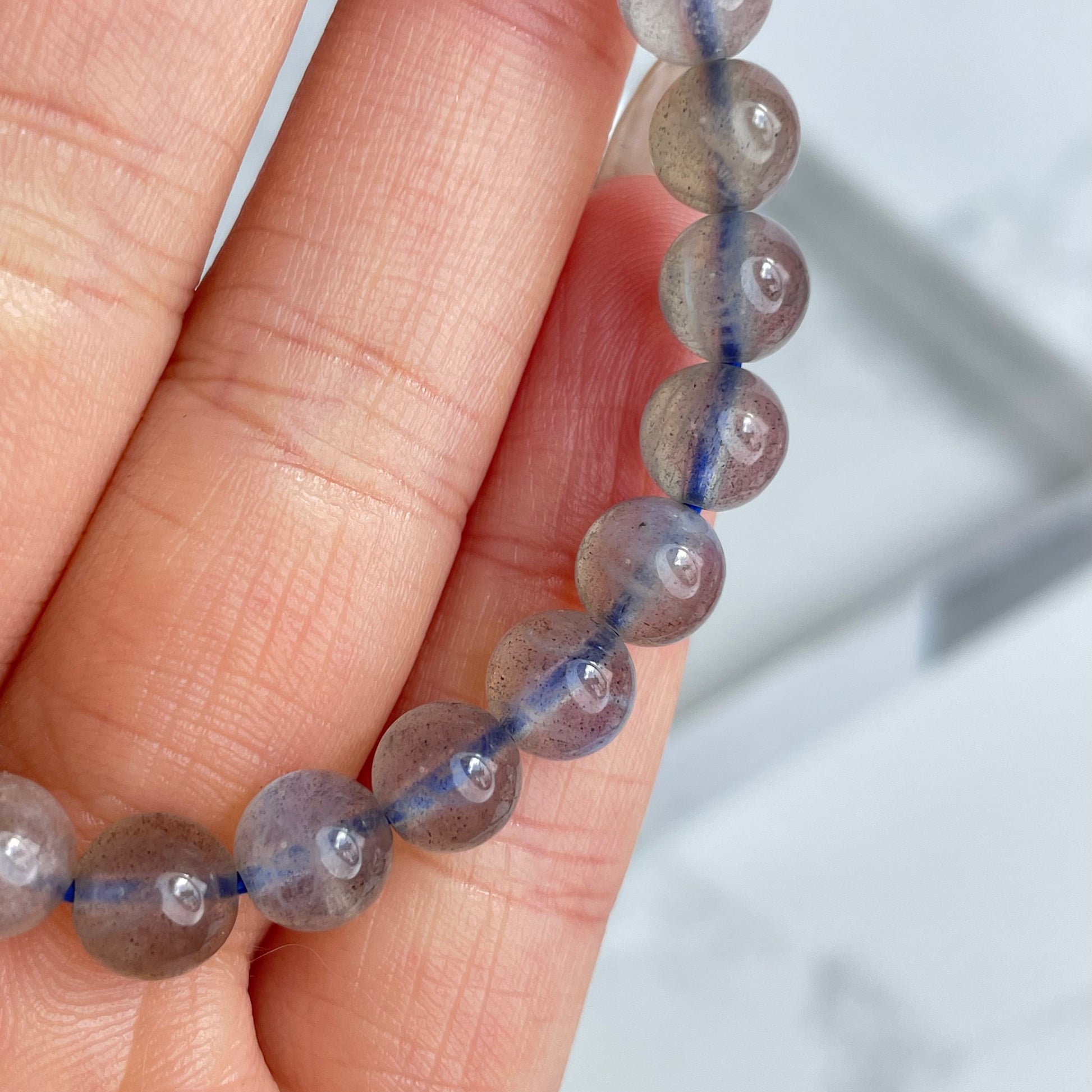 Labradorite glow bracelet with blue flashes – 6mm beads, from Madagascar. Displayed on hand and flat lay with marble background.