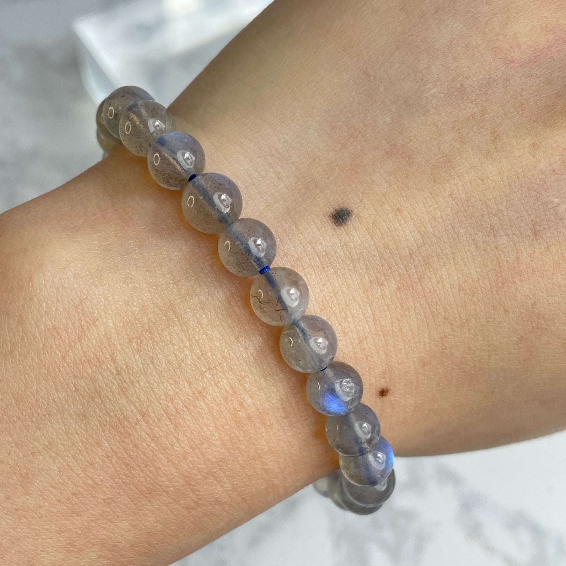 Labradorite glow bracelet with blue flashes – 6mm beads, from Madagascar. Displayed on hand and flat lay with marble background.