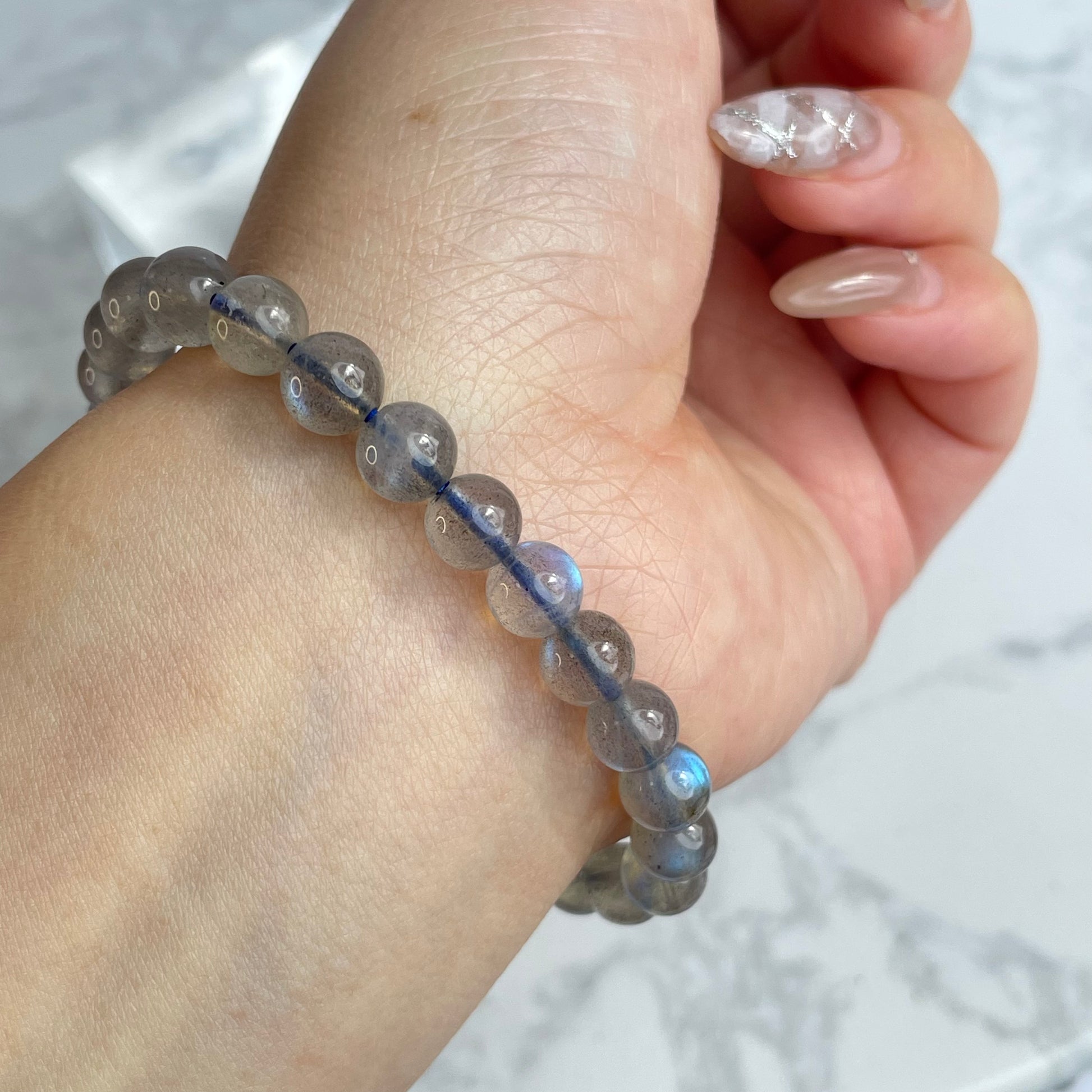 Labradorite glow bracelet with blue flashes – 6mm beads, from Madagascar. Displayed on hand and flat lay with marble background.