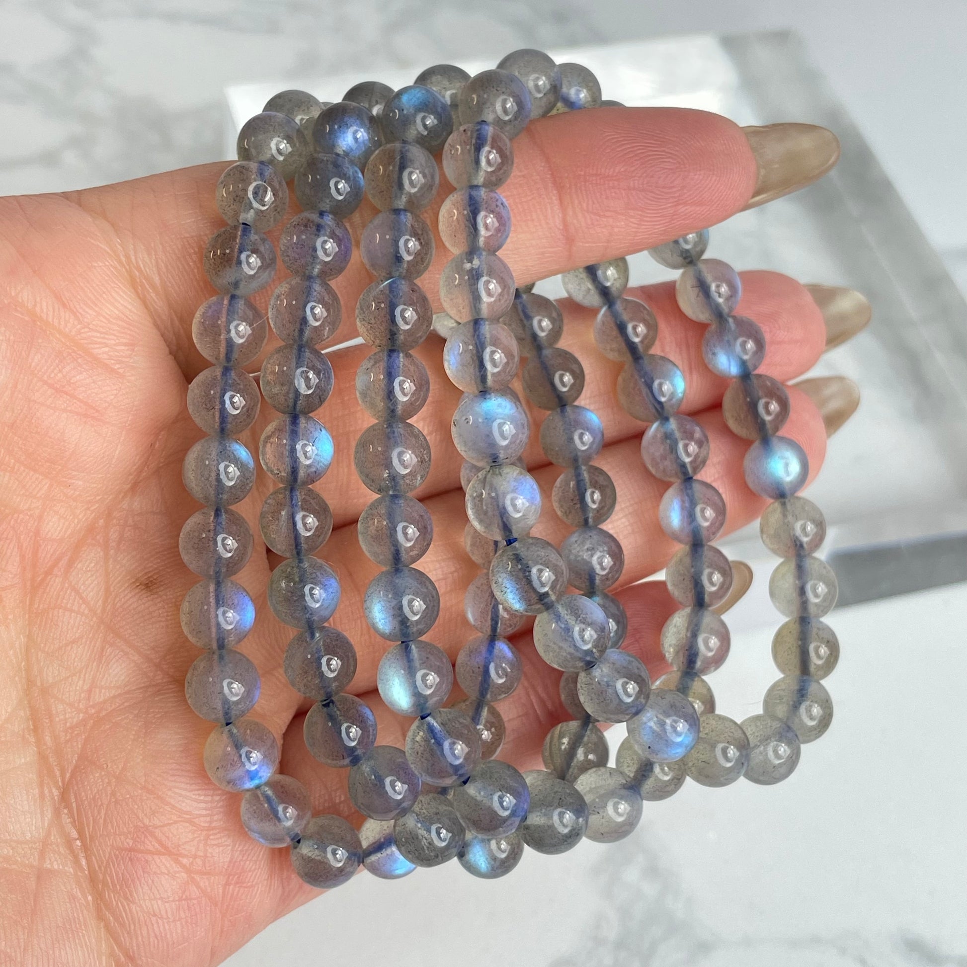 Labradorite glow bracelet with blue flashes – 6mm beads, from Madagascar. Displayed on hand and flat lay with marble background.