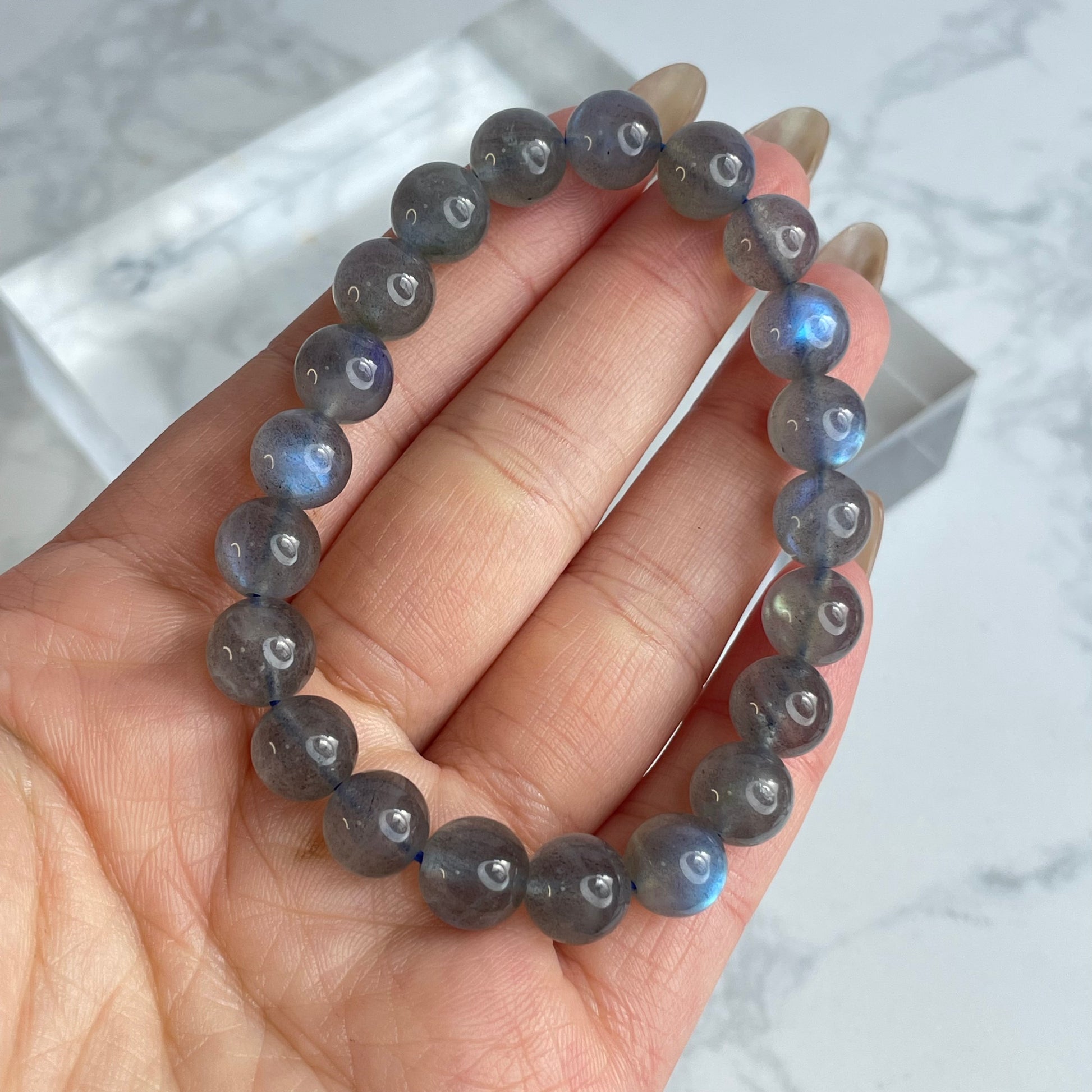 Hand holding a round bead labradorite bracelet with subtle dark gray tones and visible blue flashes under natural lighting, showcasing the moonlight glow effect.