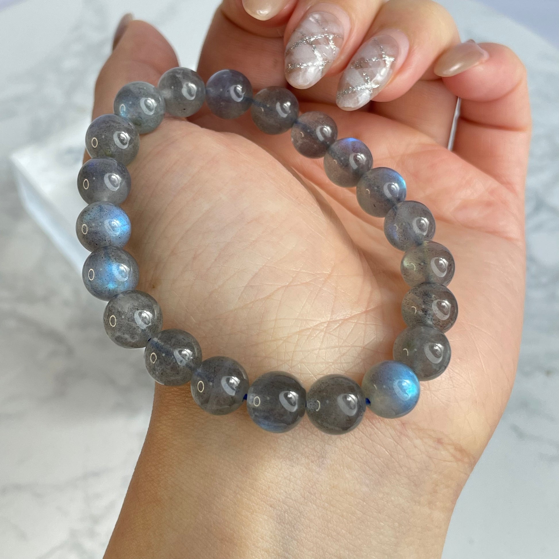 Close-up of a hand holding a Labradorite bracelet, showcasing its blue flashes and natural texture of each bead.