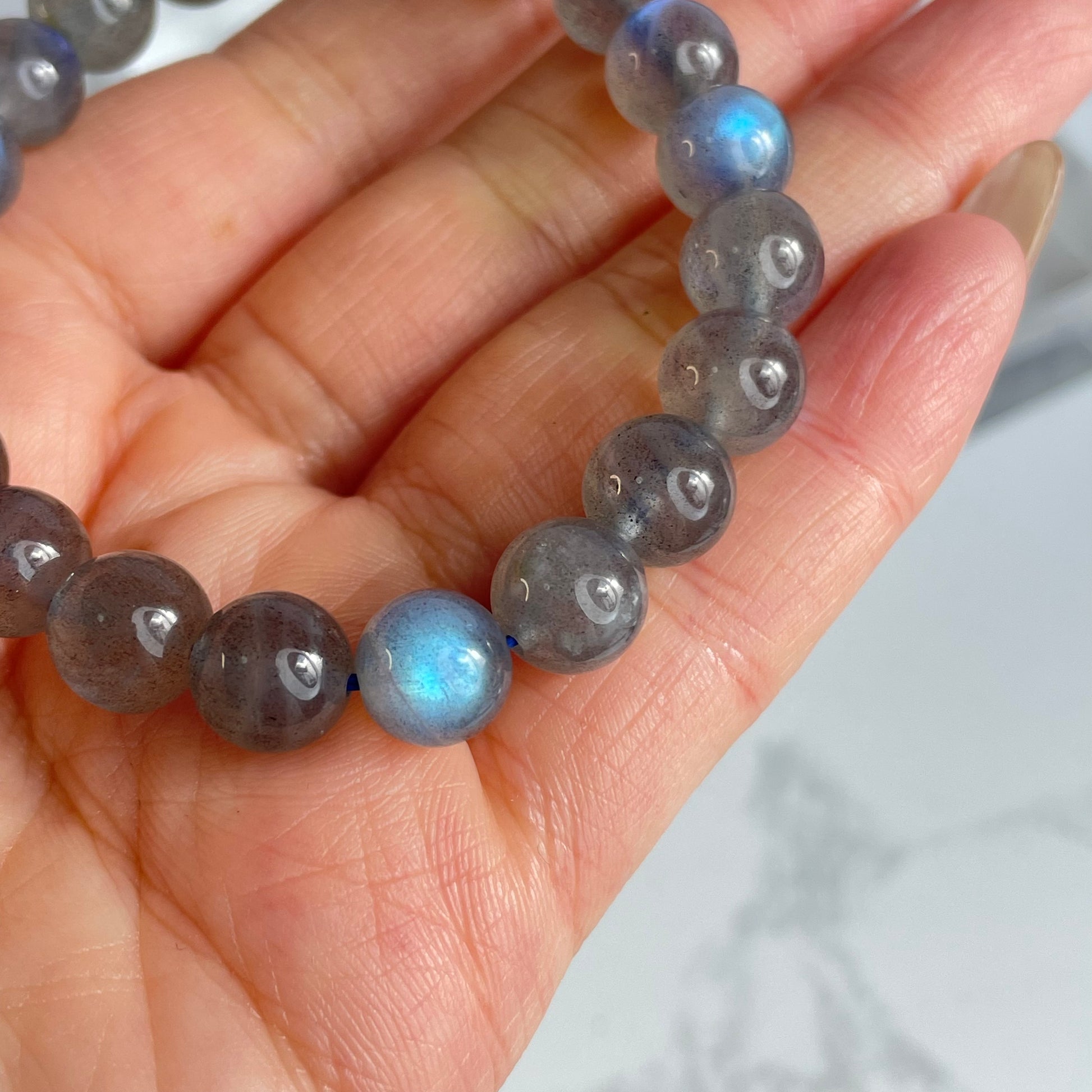 Close-up view of Labradorite bracelet showing strong blue flash on a single bead, with hand in background.