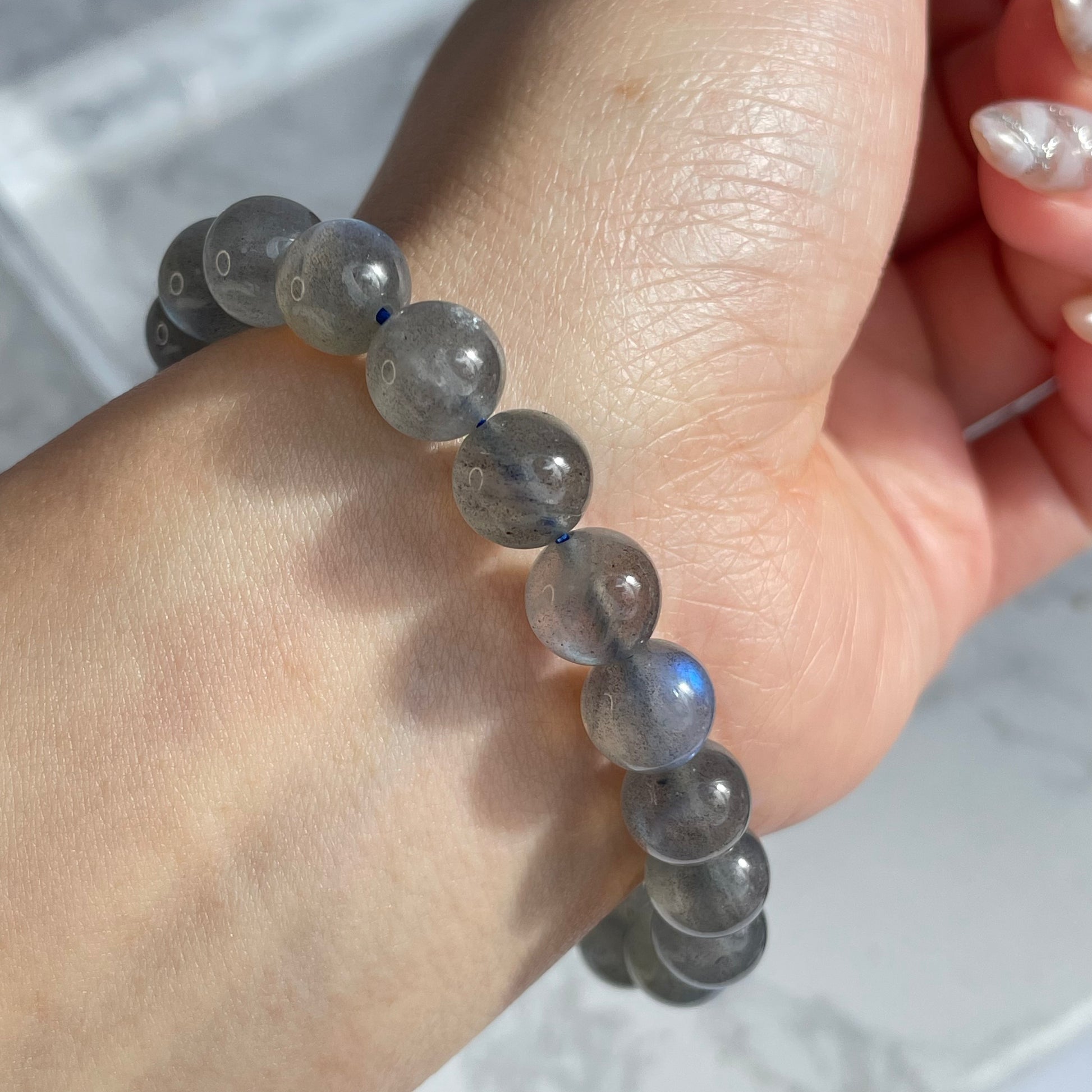 Labradorite bracelet worn on wrist, capturing soft blue flash on translucent grey beads.