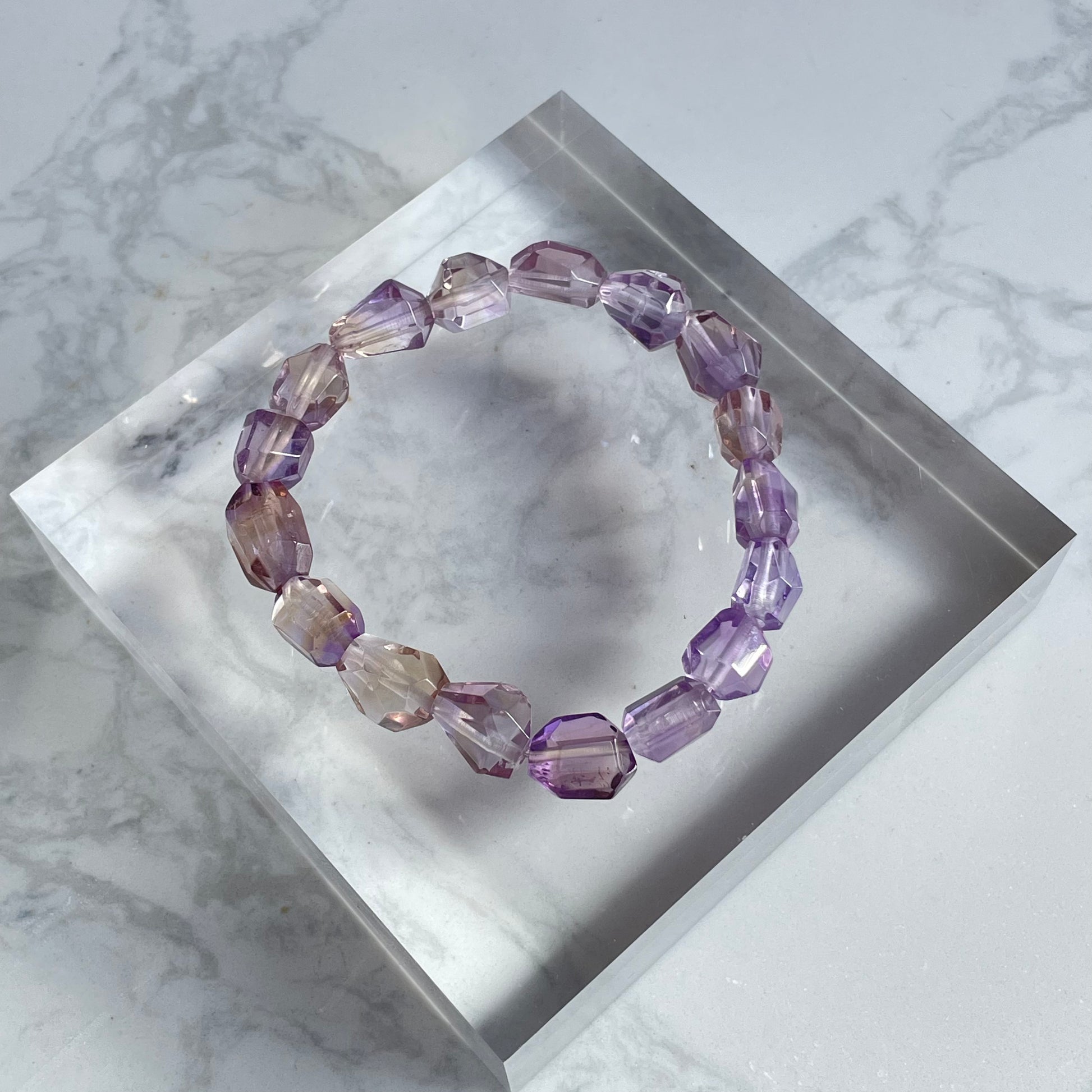 Raw-cut ametrine bracelet with natural geometric shapes, showcasing a soft blend of light purple and golden hues. Photographed on a clear crystal acrylic base.