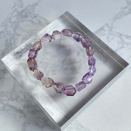 Raw-cut ametrine bracelet with natural geometric shapes, showcasing a soft blend of light purple and golden hues. Photographed on a clear crystal acrylic base.